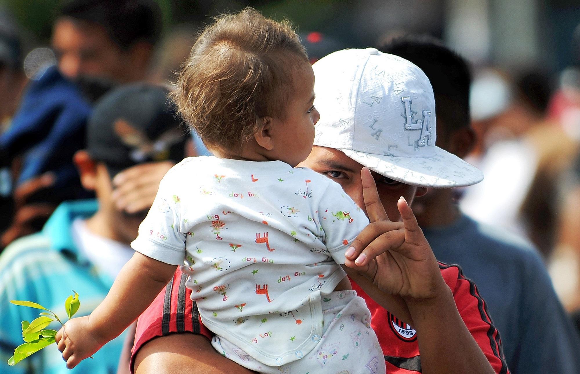 Un joven con un bebé en brazos hace con su mano la garra que simboliza la MS-13. Esta fotografía se tomó el 3 de marzo de 2010, en una marcha de pandilleros y familiares que recorrió las calles de San Salvador. Foto José Cabezas (AFP).