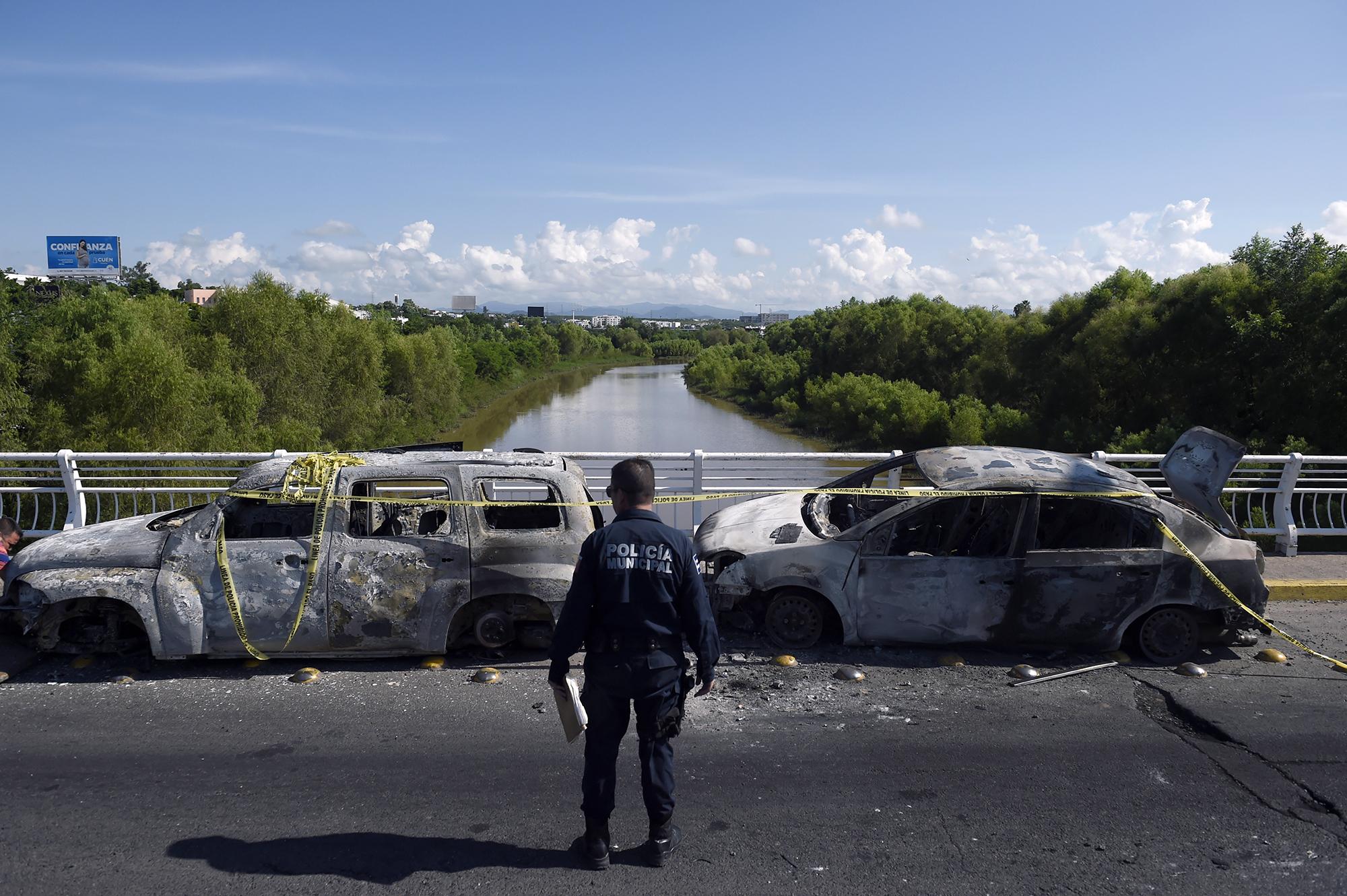 La narcoviolencia somete a México. Un policía se encuentra al lado de vehículos quemados después de que hombres fuertemente armados libraron una batalla total contra las fuerzas de seguridad mexicanas en Culiacán, estado de Sinaloa, el 18 de octubre de 2019. El presidente de México, Andrés López Obrador, enfrentó una tormenta de críticas luego de que sus fuerzas de seguridad confirmaran el arresto del hijo del capo Joaquín 
