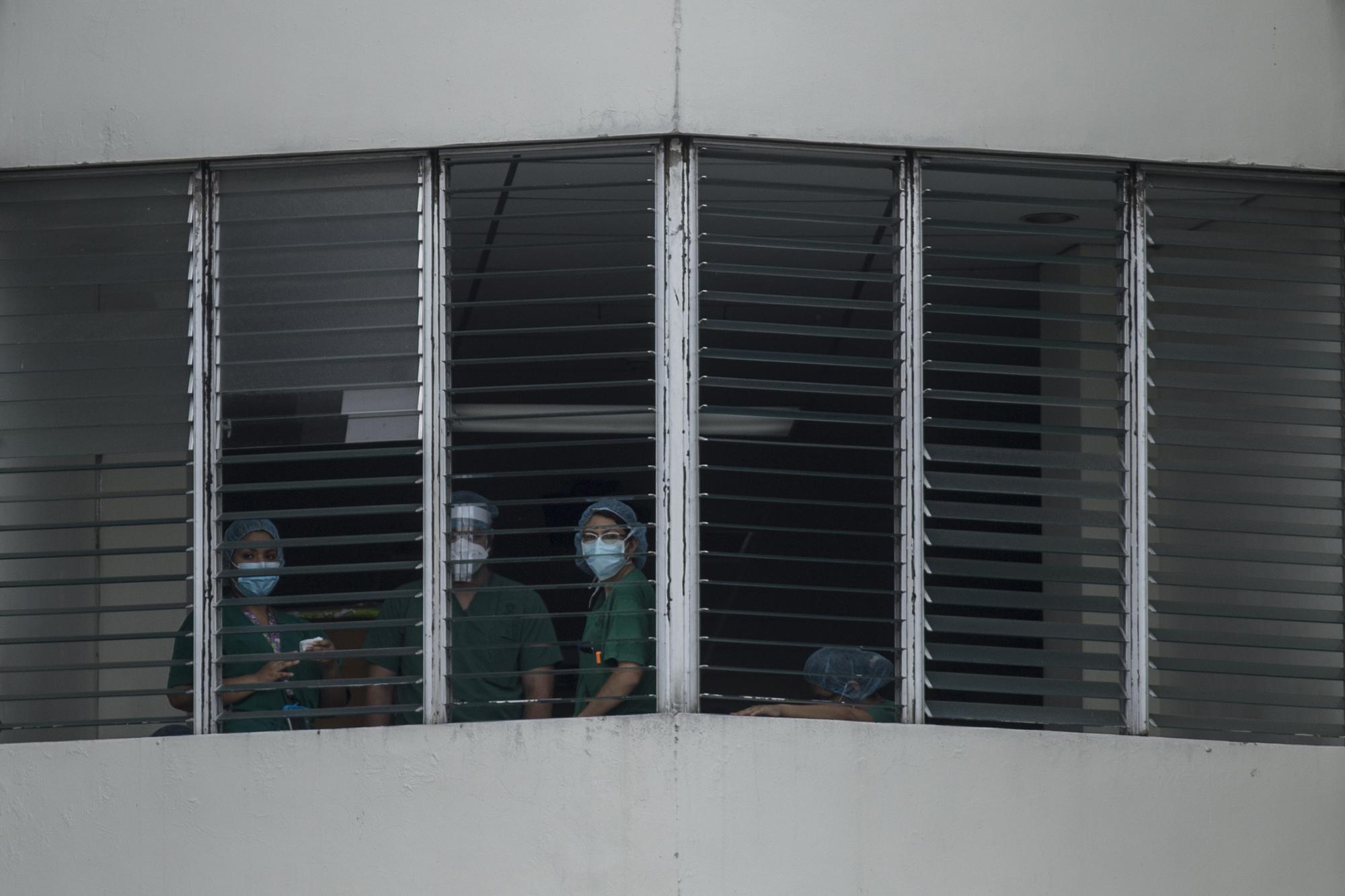 Personal médico del hospital San Rafael, en el municipio de Santa Tecla, observan hacia la plaza principal, donde un grupo de jóvenes realizaban una campaña de oración, el 18 de mayo de 2020. Foto de El Faro: Víctor Peña. 