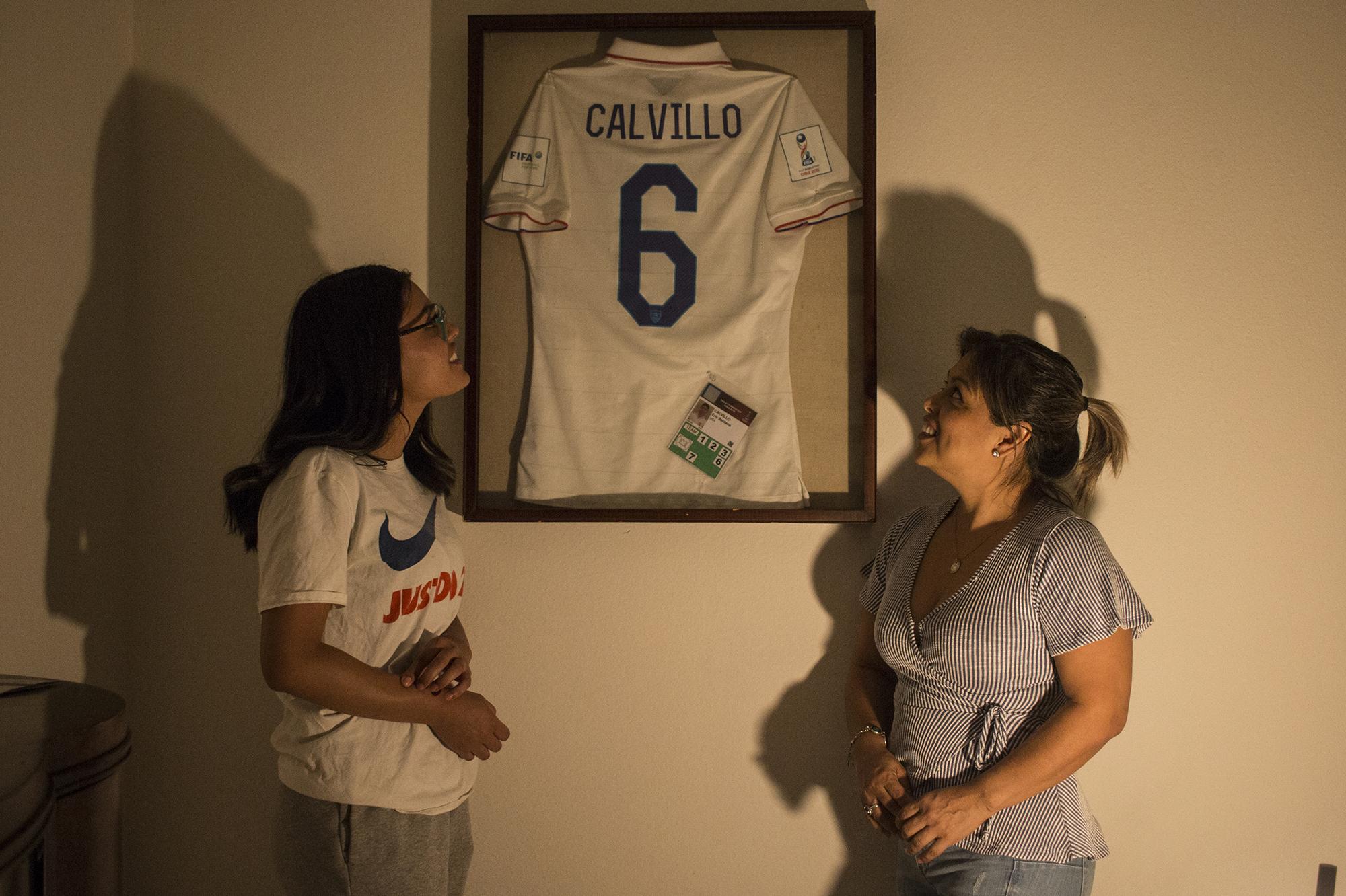 Desireé Calvillo (derecha) y su hija Giselle posan con la camiseta que Eric Calvillo usó en el mundial juvenil que disputó con Estados Unidos en el año 2015. Calvillo ahora representa a El Salvador y su madre tiene pendiente enmarcar su camiseta para ponerla al lado de esta en su residencia de Lancaster, en el condado de Los Ángeles, California. Foto de El Faro: Víctor Peña. 