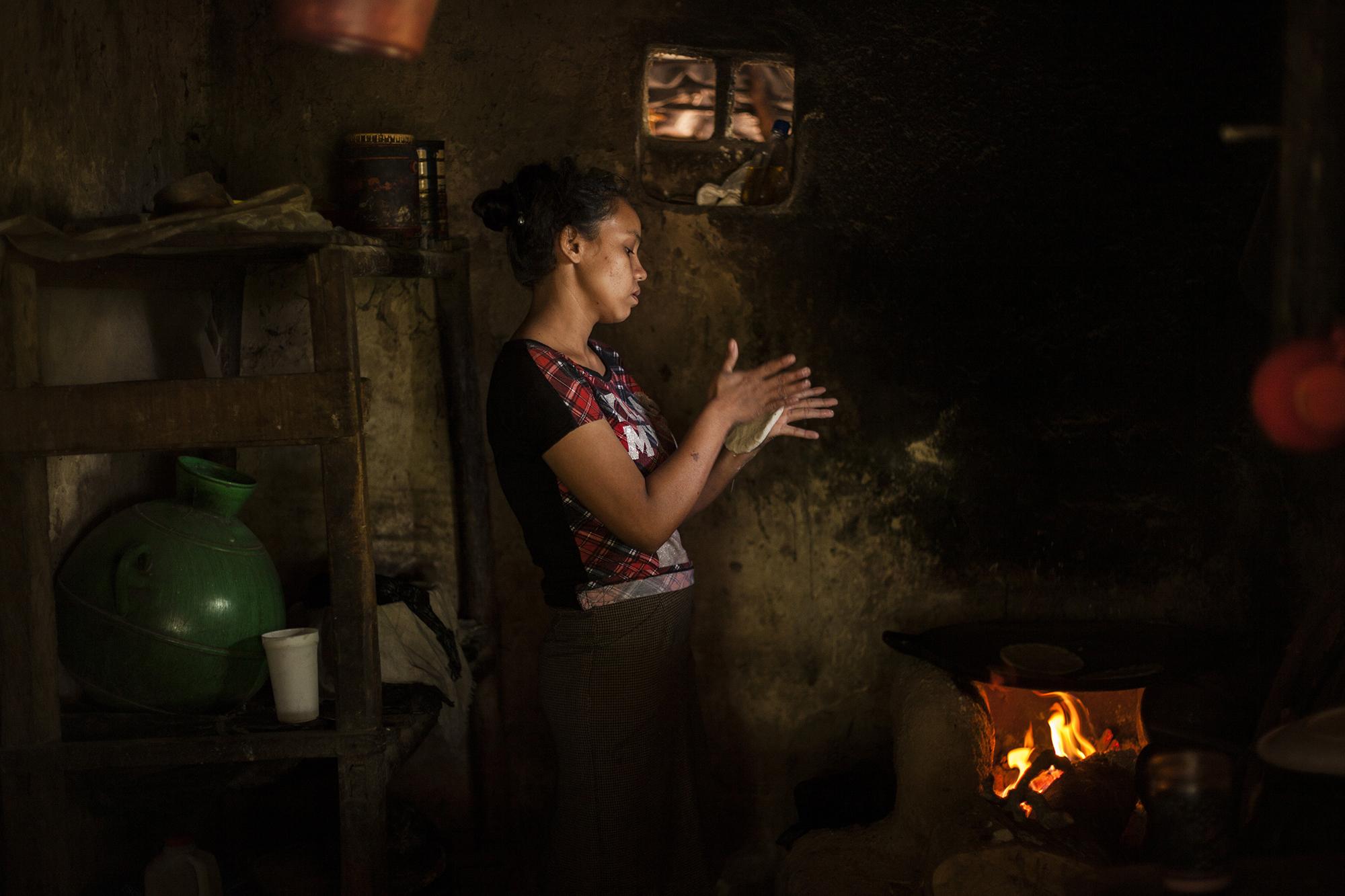 Dora Alicia Vigil (28 años) prepara el almuerzo para su familia. Asiste dos veces por semana al huerto comunitario, donde recoge alimentos. Dora habita en una de las 18 casas que componen la parte baja del caserío El Volcán y que, como todas las demás, carece del servicio de energía eléctrica.