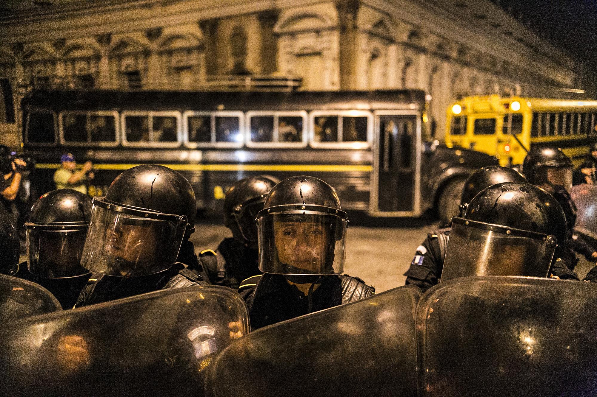 Antimotines bloquean el paso de periodistas y manifestantes sobre la 10ª calle mientras que los diputados, atrás, abandonan el congreso en tres buses. Según informo un medio guatemalteco, uno de los diputados tiró gas a manifestantes y periodistas desde la ventana del bus.