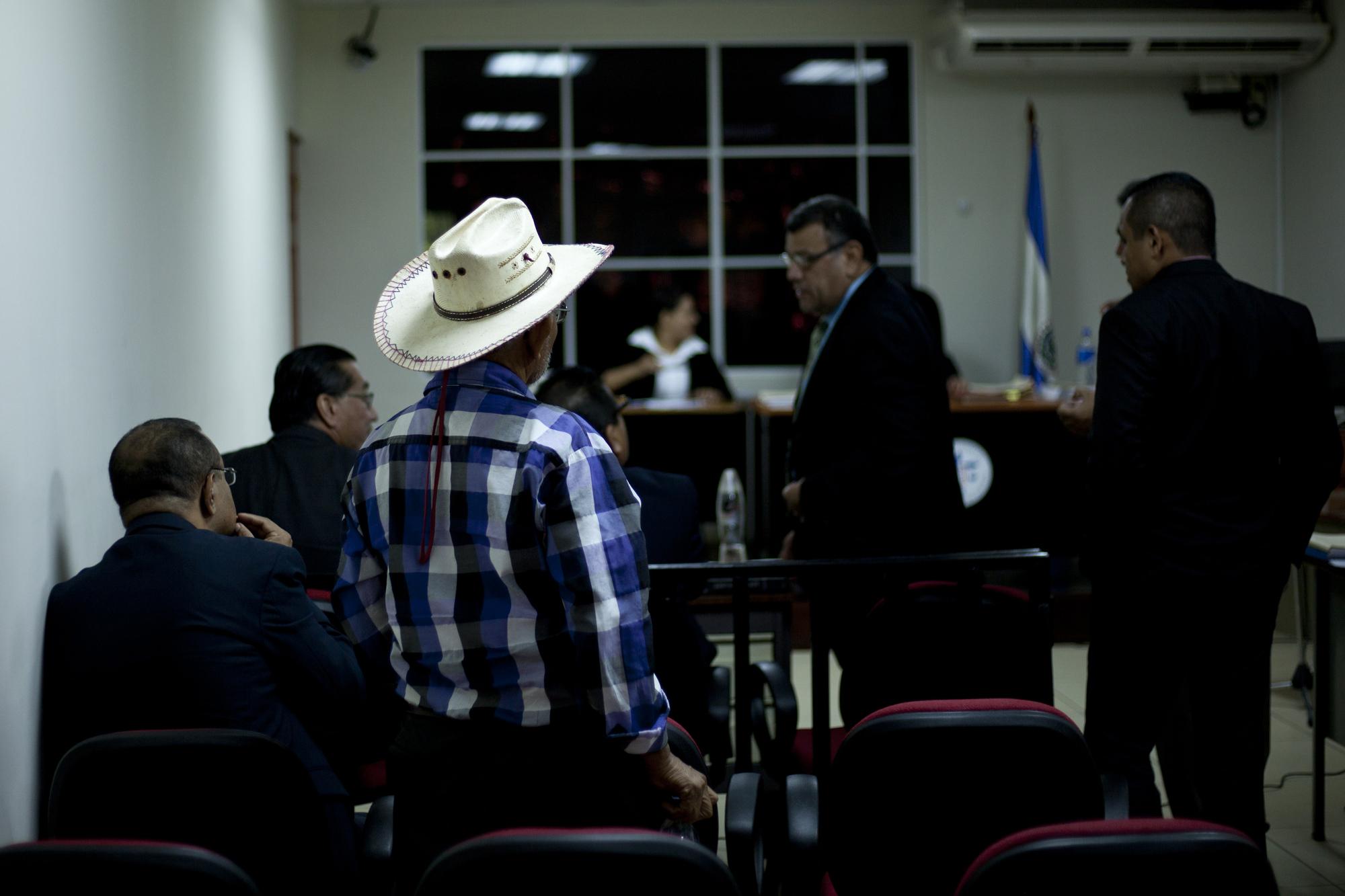 Un hombre espera que Lucila Romero (fuera de foco) empiece su testimonio, durante la audiencia del caso El Mozote, en el juzgado de San Francisco Gotera, Morazán. Al fondo, los fiscales y acusadores. Foto de El Faro, por Víctor Peña.