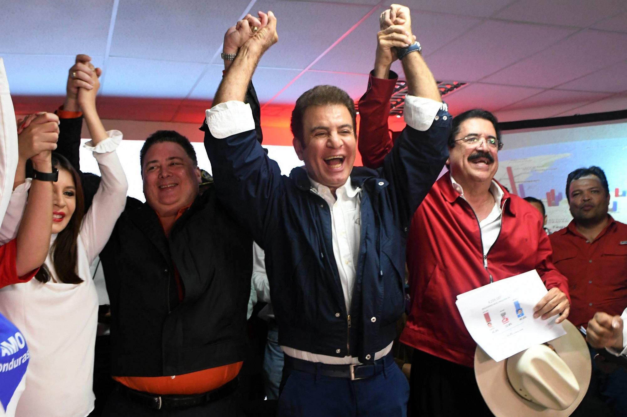 Al centro, Salvador Nasralla, del partido Alianza Opositora, celebra los resultados oficiales del TSE que con el 57 % escrutado lo perfilan como ganador de las presidenciales hondureñas. A la izquierda de Nasralla, sombrero en mano, el expresidente Manuel Zelaya, cuya mandato fue abortado en junio de 2009 por un golpe de Estado. Foto Orlando Sierra (AFP).