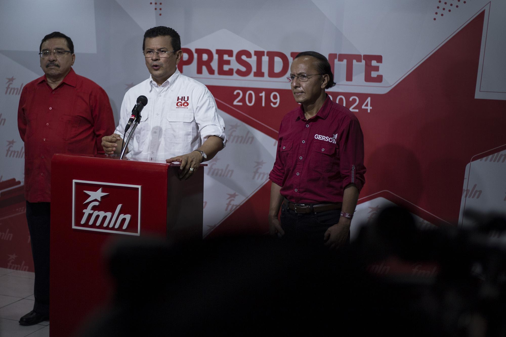 Gerson Martínez frente a la conferencia de prensa, en la sede conocida como 1316, mientras su contrincante Hugo Martínez ofrece un discurso, después de que Medardo González lo proclamara ganador de las elecciones internas del FMLN. Foto de El Faro, por Víctor Peña.