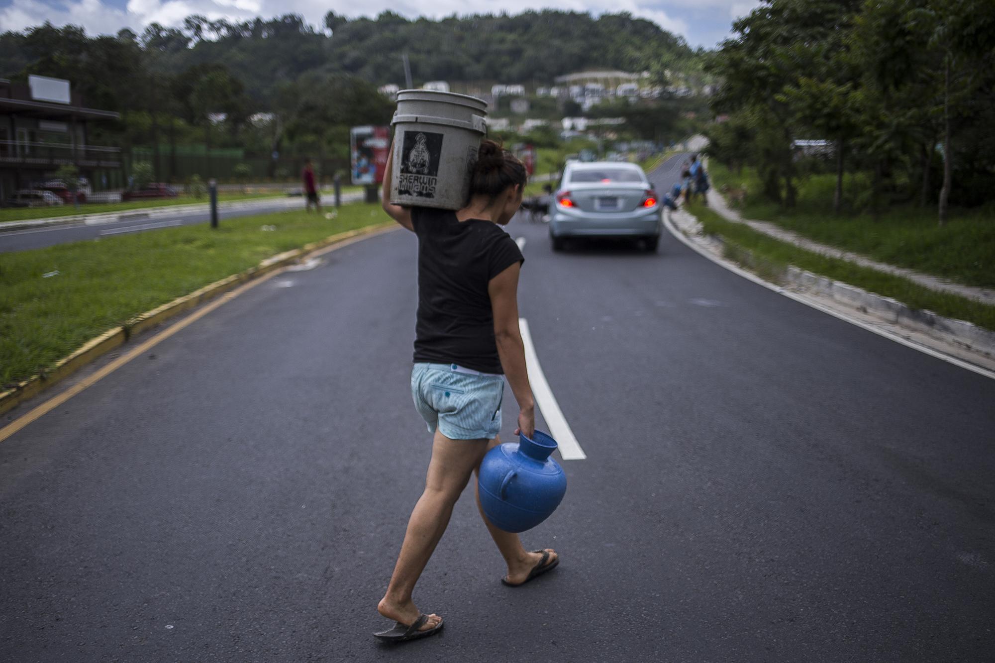 Una habitante de la comunidad La Esperanza, en Nuevo Cuscatlán, recorre el bulevar Cuscatlán con el agua que ha logrado recolectar del pozo municipal cercano a su vivienda. Foto de El Faro, por Víctor Peña.