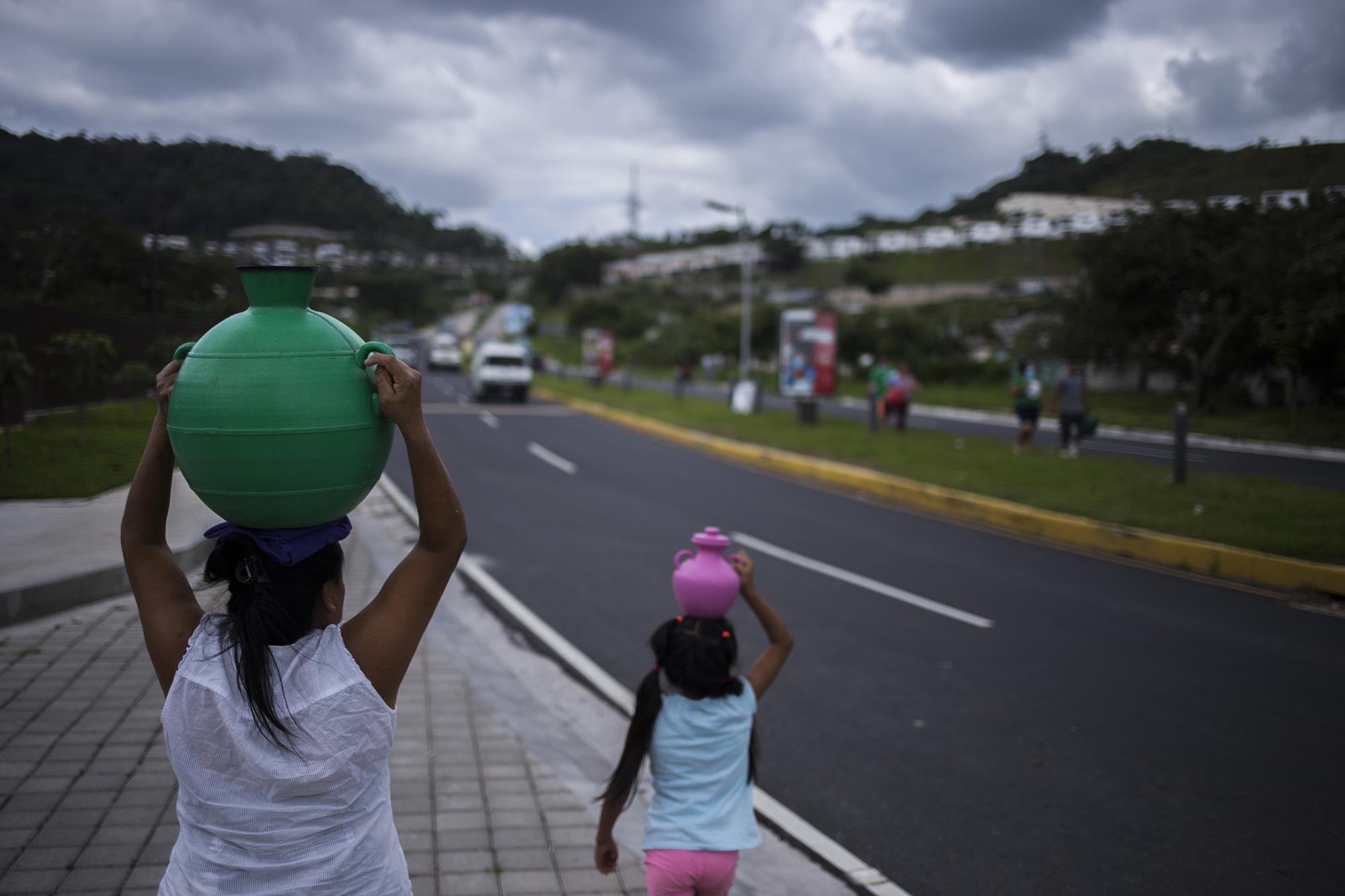 Blanca Lilian Miranda, de 49 años, recorre el bulevar Cuscatlán junto a Fernanda, su nieta, quien le ayuda a la recolección de agua desde el pozo de la Alcaldía Municipal de Nuevo Cuscatlán. Foto de El Faro, por Víctor Peña.