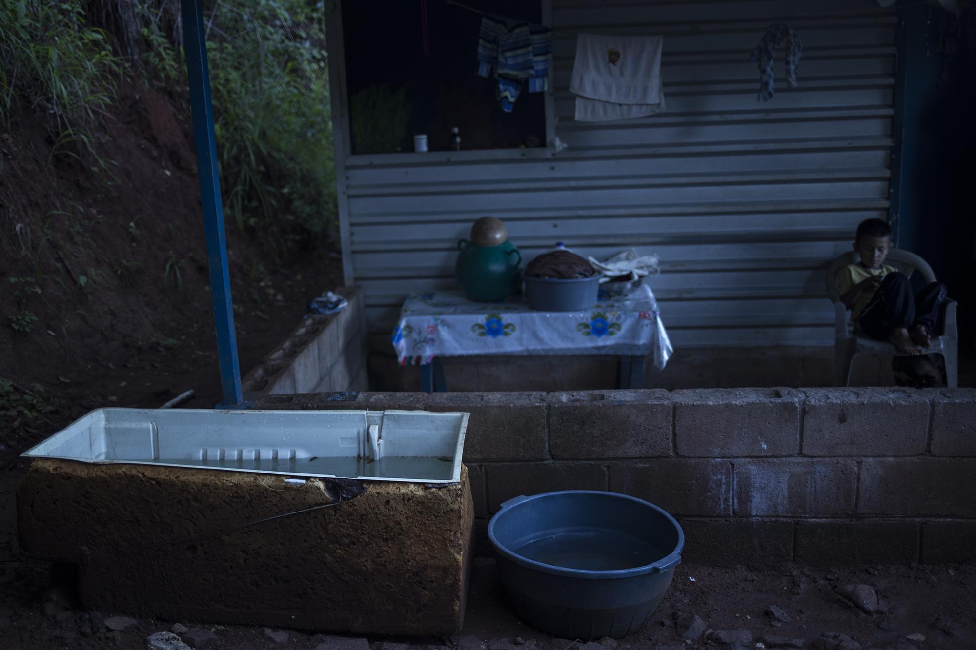 La casa de Cristian David Orellana, de seis años, en el cantón La Uvilla, es casi la última en lo alto de la comunidad. Para obtener un poco de agua, su madre ha colocado los escombros de una refrigeradora, donde almacena lo que baja del techo cuando llueve. Cristian vive en una casa fabricada con láminas, junto a sus padres y su hermana menor.