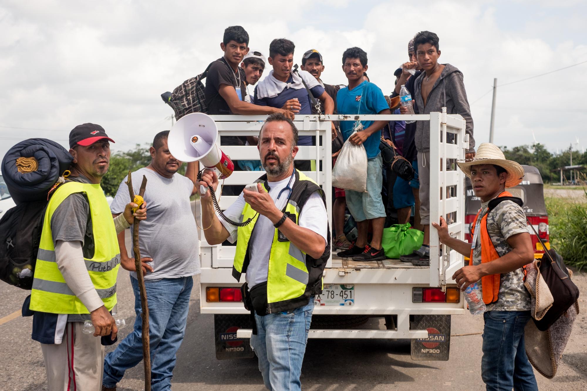 El doctor Manuel Valenzuela  (centro con chaleco verde) es ejerce en el Paso, Texas, pero ahora acompaña la caravana como voluntario. En la foto, se encarga de conseguir aventones para los migrantes hacia la ciudad de Matías Romero, Oaxaca. 1 de noviembre de 2018. Foto: Fred Ramos.