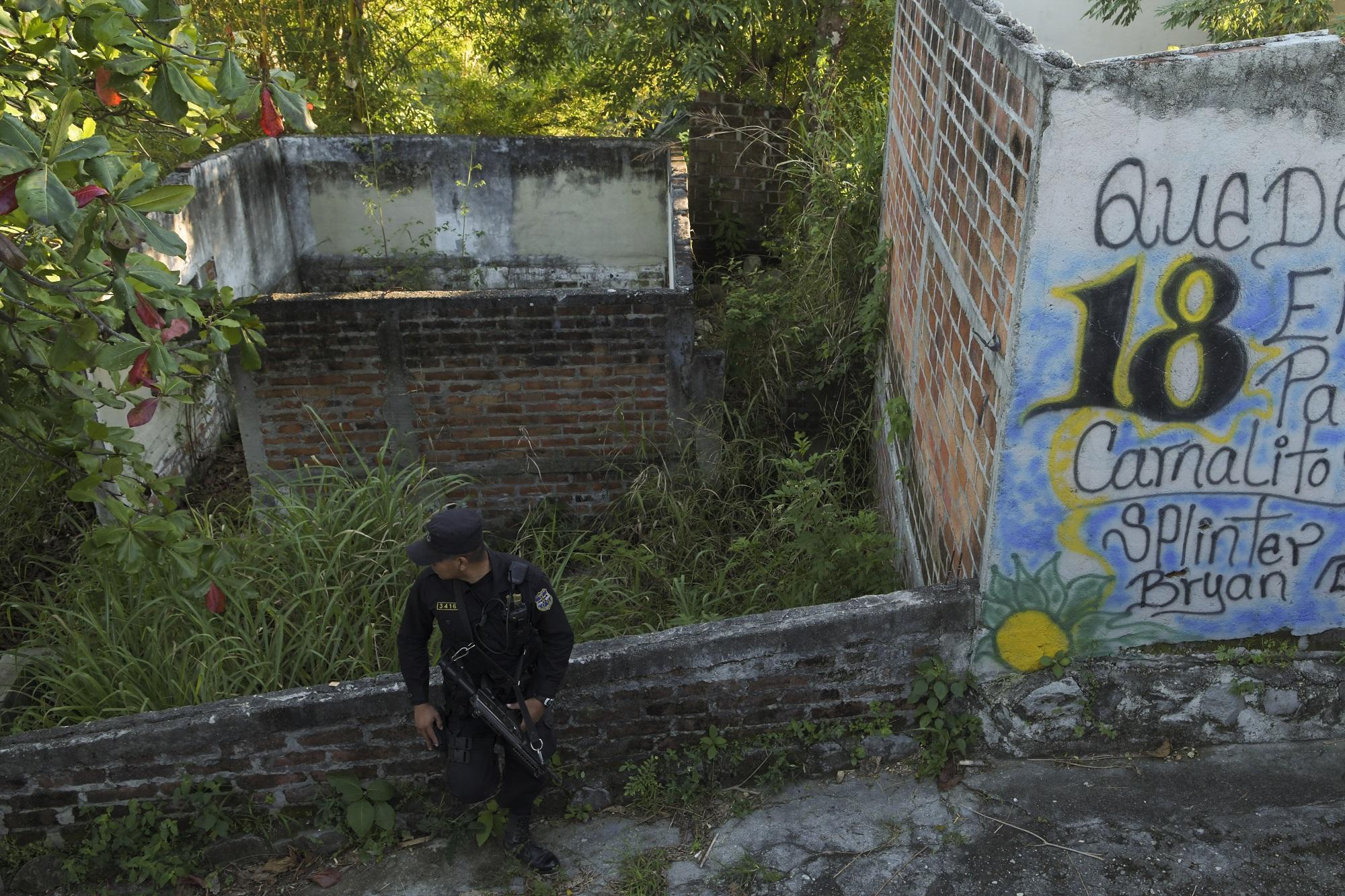 Un agente de la PNC vigila una colonia del municipio de San Martín apostado junto a un  placazo  del Barrio 18. Foto Marvin Recinos (AFP).