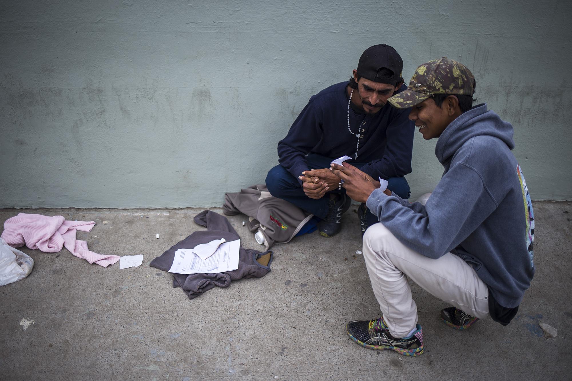 José Castillo, de 30 años (Izq.), y Rudy Efraín Martínez, de 20, han llegado por tercera vez al Proyecto Salesiano de Tijuana, el 5 de diciembre, donde se desarrolla una feria de empleo. Ambos sonríen al leer sus documentos de aplicación para recibir, una semana después, un carné de trabajo. aseguran que huyeron de la extrema violencia en el municipio de Danlí, departamento de El Paraíso, Honduras. Buscan ensamblar y pintar carros en Tijuana.