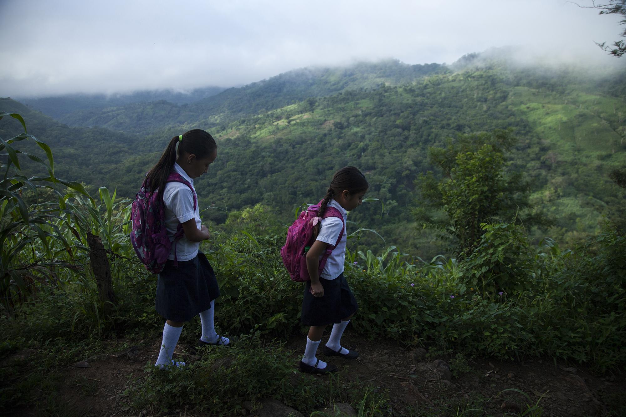 Alumnas del Centro Escolar Caserío Las Anonas, en el cantón Tijeretas, del municipio de Torola, caminan hacia su escuela. Para llegar a esta escuela remota del departamento de Morazán, los alumnos recorren alrededor de 40 minutos por caminos estrechos, en medio de montes y cultivos de máiz con los que subsiste su comunidad. 20 de octubre de 2017. Foto: Víctor Peña.