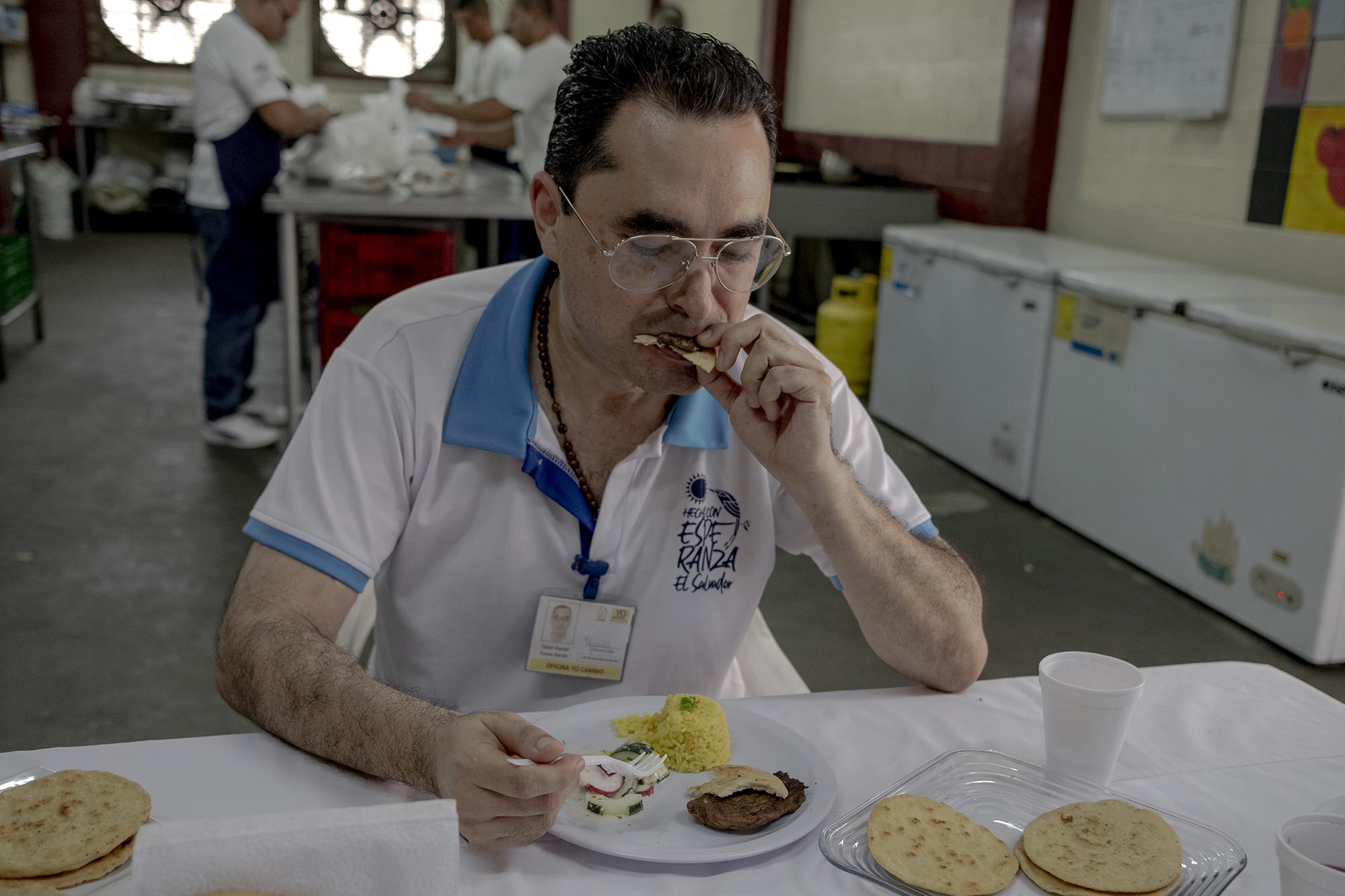 Funes almuerza en el interior de la cocina. Recibe la misma alimentación que los demás reos. La empresa Food Tech es la encargada de preparla y los reos son los encargados de servirla. Otra opción de comida en Mariona, para aquellos que reciben dinero, es una especie de cafetería cuya cocina es manejada por internos. Cada reo tiene derecho a recibir de sus familiares una remesa electrónica de hasta $150 por mes. En la imagen, Funes come alimentos comprados en la cocina. 