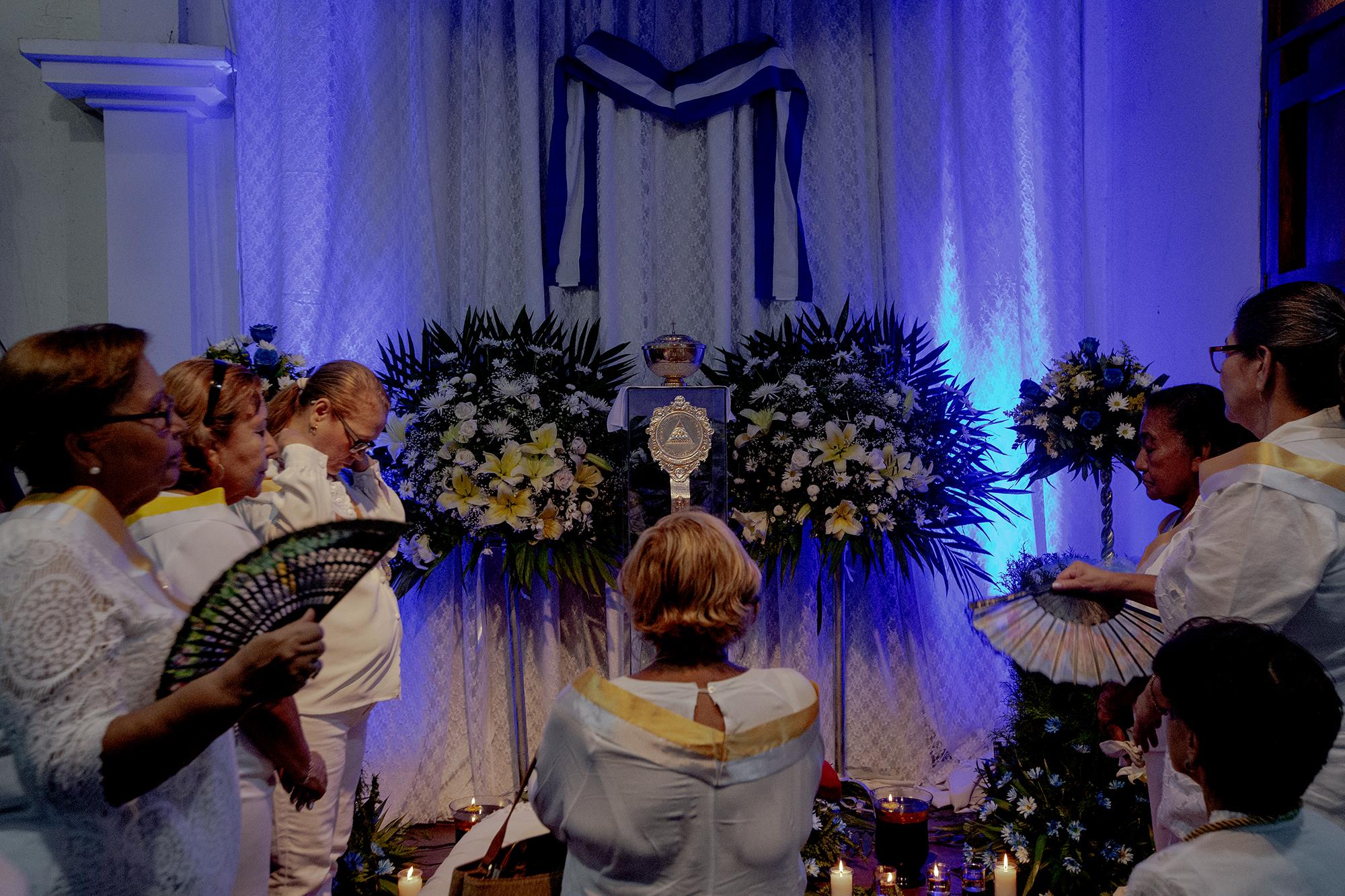 Feligreses rezan y fotografían el altar del santísimo en la iglesia San Miguel, de Masaya. El padre Edwin Román decoró el altar con la bandera y el escudo de Nicaragua, símbolos utilizados durante las protestas contra el régimen de Ortega. Algunos feligreses aseguran que sufren constante acoso policial y otros dicen que incluso han teido que abandonar sus casas.