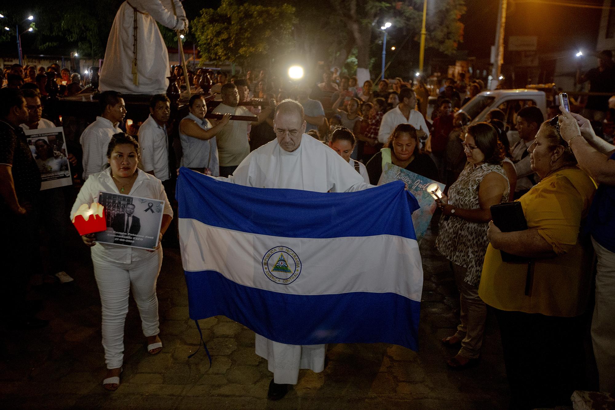 El padre Edwin Román, párroco de la Iglesia San Miguel en Masaya, cargo una bandera de Nicaragua durante la procesión del silencio que se realiza el  jueves santo. En la procesión también participaron familiares de los muertos y de los presos políticos. Debido a la labor humanitaria que Román realiza, ha recibido amenazas de muerte, es por eso que  desde junio del año pasado posee medidas cautelares por parte de la CIDH. 18 de abril de 2019. Foto: Fred Ramos