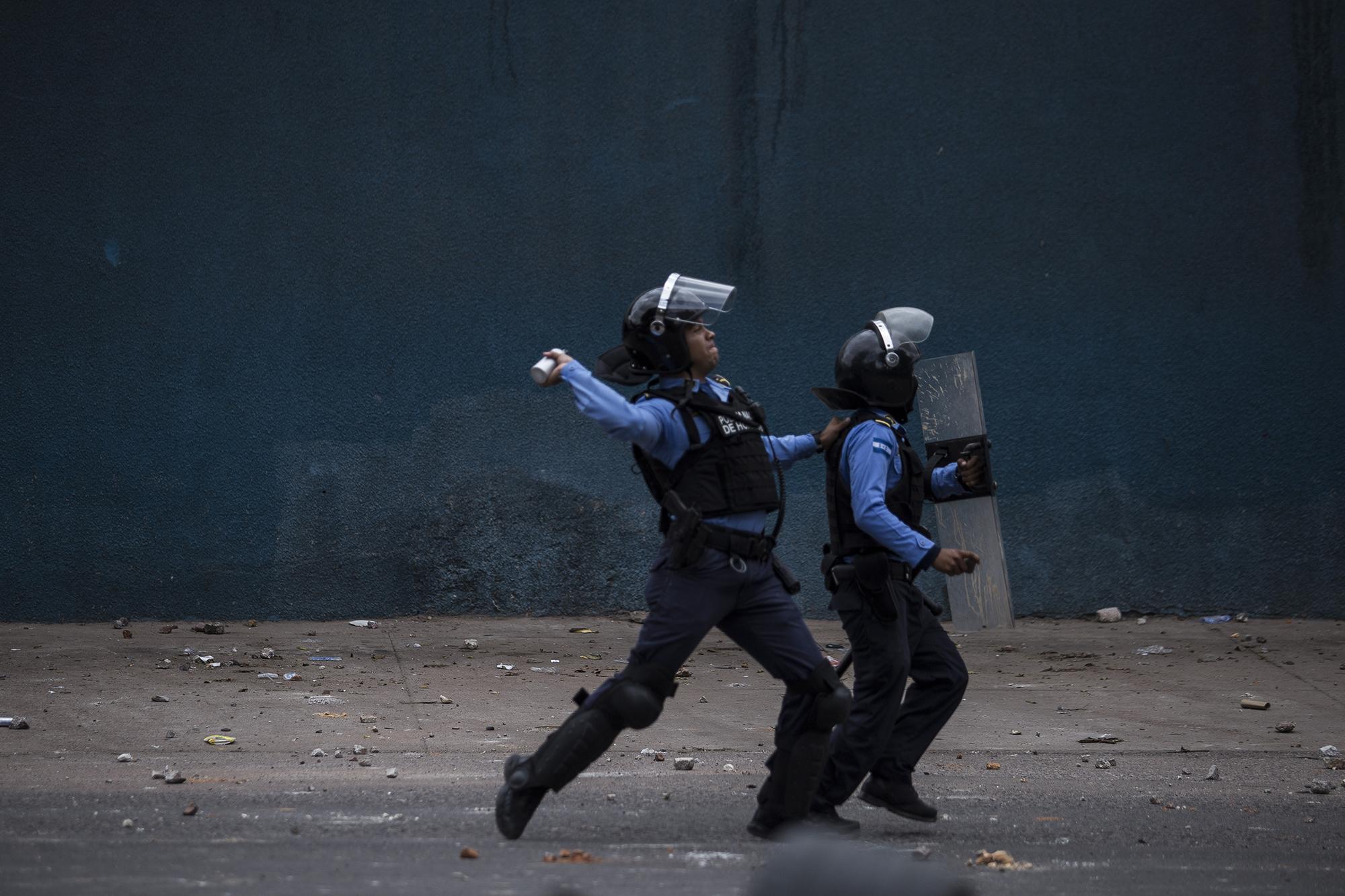 Un miembro de la policía anti motines de Honduras lanza una bomba lacrimógena a los estudiantes del Instituto Técnico Honduras que protestaban frente al estadio Emilio Larach, en la colonia Kennedy, en la ciudad de Tegucigalpa. Foto: Víctor Peña.