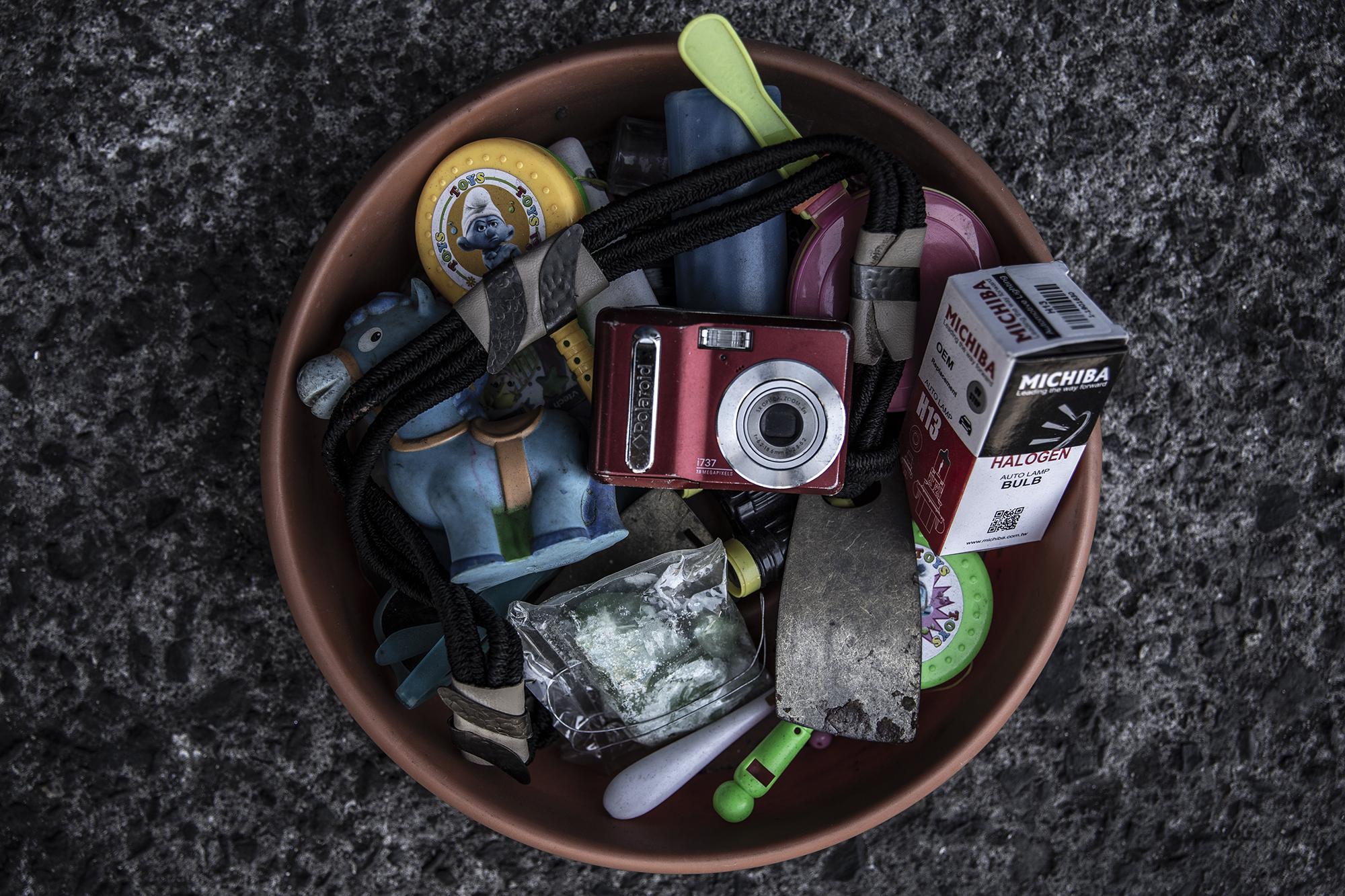 Nelson Molina recolecta cosas de sus familiares y amigos. A veces, compra pequeños objetos que según él podrá vender a buen precio. El precio del recipiente de la imagen, con todos los artefactos, es de $2. La cámara digital no funciona. Hay juguetes rotos y hasta un aromatizante para baño.