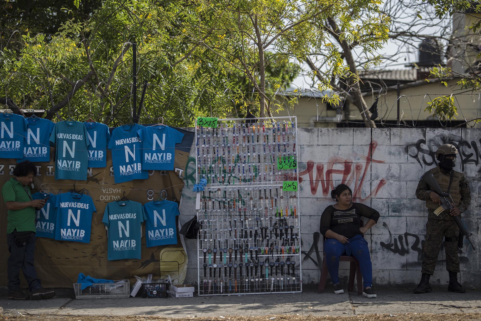 La concentración de simpatizantes organizada por el Gobierno atrajo numerosos puestos de venta. En la imagen, camisetas con el nombre del presidente se venden a pocos metros de un soldado armado, a pocos metros de la Asamblea legislativa. Foto El Faro. Víctor Peña.