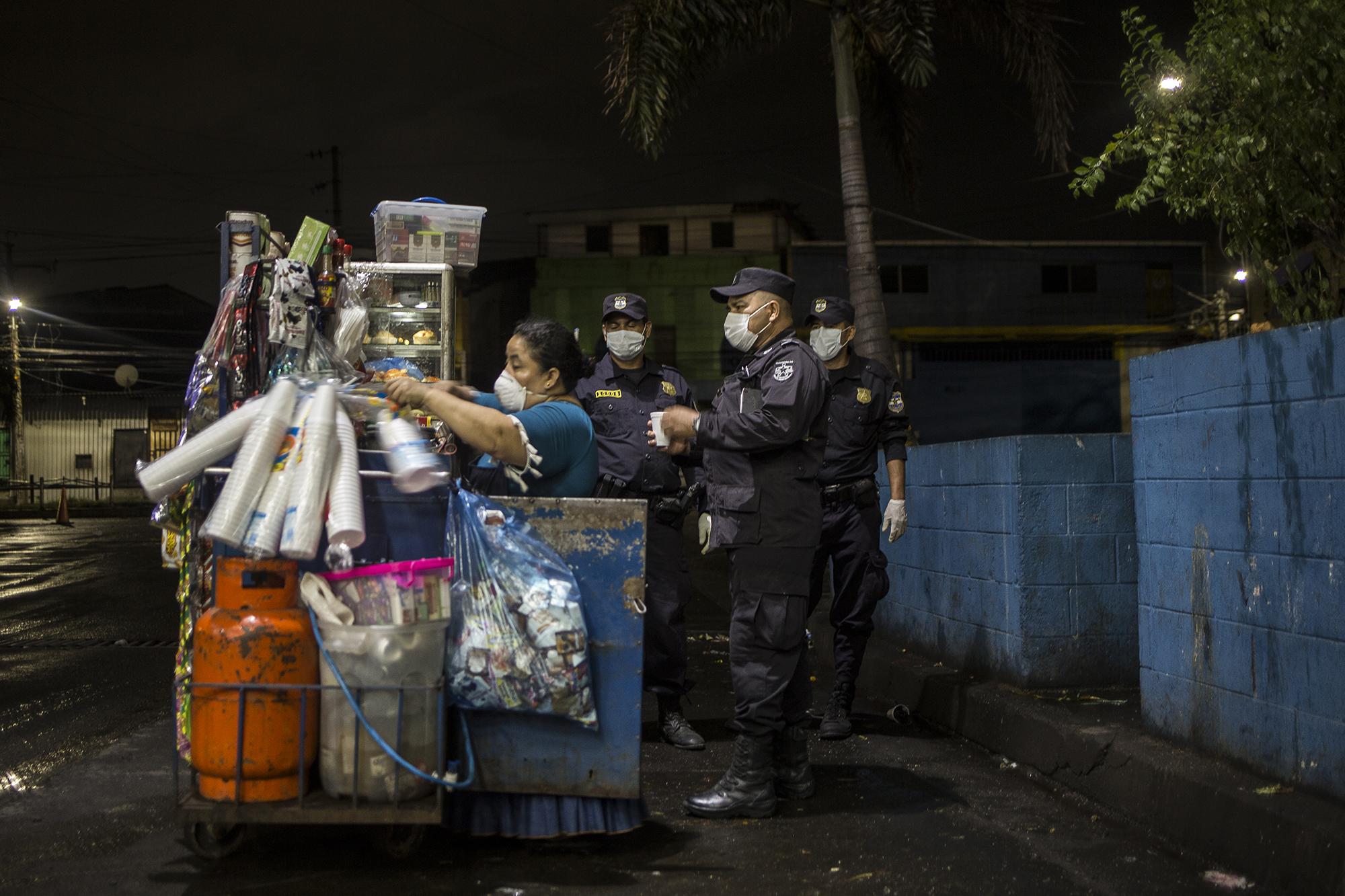 “La PNC me saco del mercado. Nos va a afectar, pero si es bueno para nuestra salud, ¿qué se va a hacer?”, dijo Johana Recinos, de 37 años, mientras repartía café a unos agentes de la Policía la noche de este sábado 21, previo al anuncio oficial de el presidente. Recinos vende sopas, café, galletas, cigarros y pan dulce en los alrededores de La Tiendona, la central de abastos de frutas y verduras de San Salvador. Es madre soltera de tres hijos, y trabaja todos días hasta la 1:00 de la mañana. Foto de El Faro: Víctor Peña.