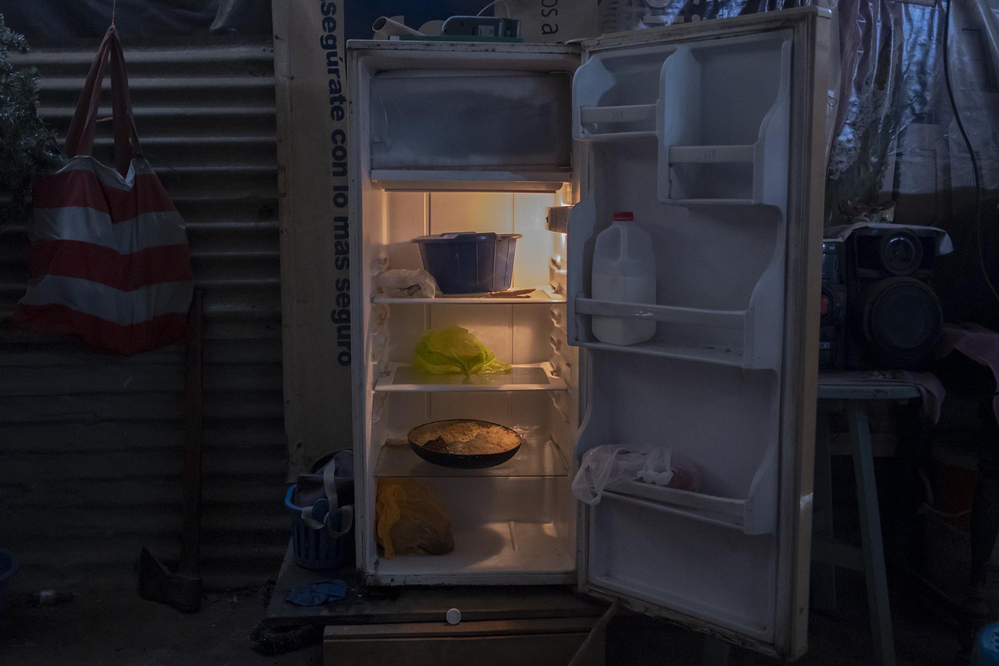 Refrigerador de una familia de la comunidad El Espino. Su contenido es: una sartén con arroz, un litro de leche, un recipiente con mangos y unas bolsas vacías. Esta casa está construida con lámina y su suelo es de tierra. La familia, compuesta por cuatro personas, subsistía de la venta de almuerzos a algunos empleados del Sistema de Integración Centroamericano, cuyas oficinas están cerca. Desde que se impuso la cuarentena domiciliar, el 21 de marzo, dejaron de vender almuerzos. Ahora, con los alimentos escaseando, en la casa solo se venden tortillas a los habitantes de la comunidad. El refrigerador guarda los alimentos para tres mujeres adultas y un niño.