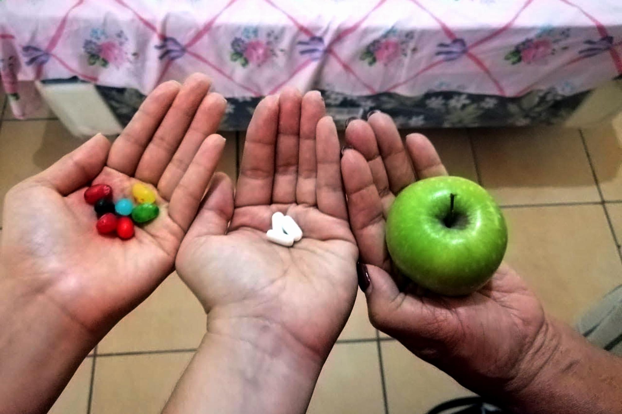 Los dulces que Aura traía para su sobrina se convirtieron en alivio para el antojo de las tres mujeres del cuarto 13 del hotel La Palma. El zinc que María Magdalena llevaba para fortalecer sus defensas fue repartido. Y consiguieron que una manzana llegara hasta el cuarto desde la tienda de enfrente del hotel. Las mujeres del cuarto 13 muestran sus tesoros de cuarentena. Foto de El Faro: María Luz Nóchez.