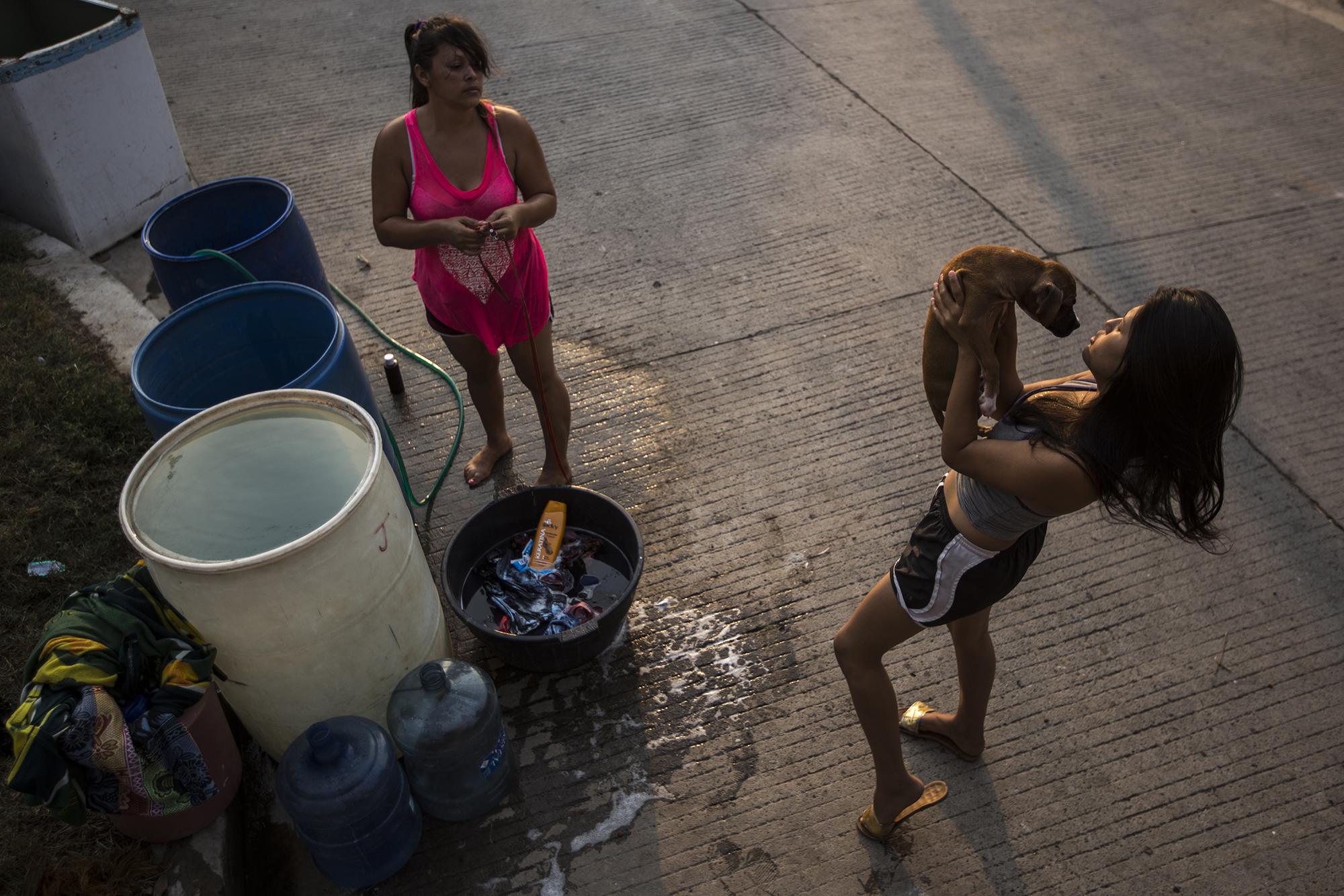 Jenny Rivas, de 32 años, y su hija Daniela, de 16, bañan a su perro y lavan sus ropas sobre la calle principal de la colonia Divina Providencia, del municipio de Apastepeque, en el departamento de San Vicente, donde el circo Wonder Boys pasa la emergencia. Madre e hija trabajan para el circo. Son bailarinas y acróbatas. Todos los martes tienen acceso al agua potable. Los demás días deben pagar $1.50 por cada barril que consuman para cubrir sus necesidades. Desde el 10 de marzo, como otros artistas, ellas no tienen ingresos económicos. 