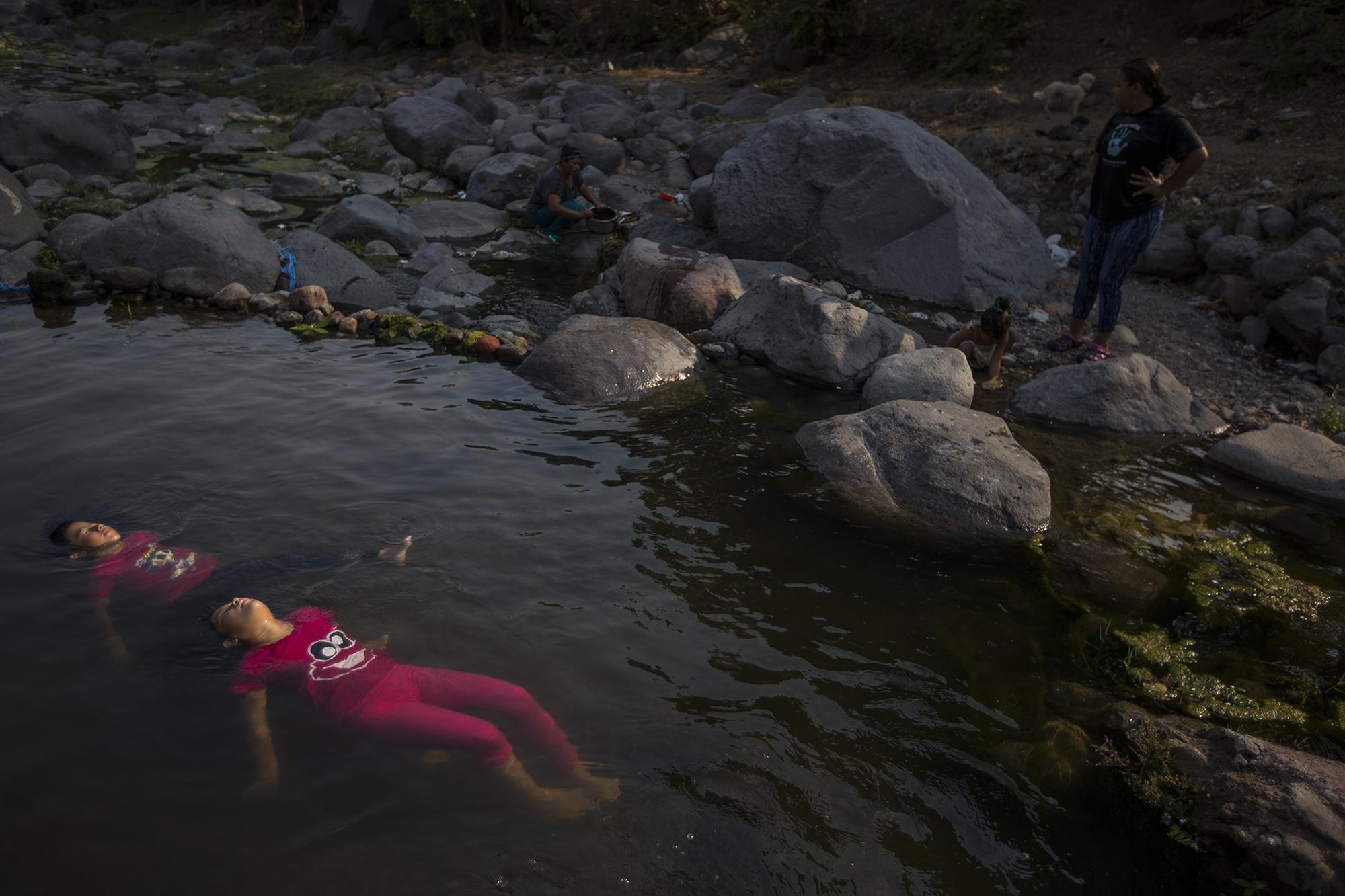 Nahomy y Miriam son gimnastas del circo de su padre. Toman un baño en una piscina improvisada que armaron con piedras y plástico, en el cauce del río Acahuapa, que recorre la ciudad de San Vicente. Al fondo, Yesenia, su madre, lava los utensilios para comer. En el Circo de Cirilo hay 15 personas. Bajan cada tarde al río para bañarse y lavar sus ropas. Pese a todo, aseguran sentirse afortunados de que la emergencia los haya sorprendido en este lugar.