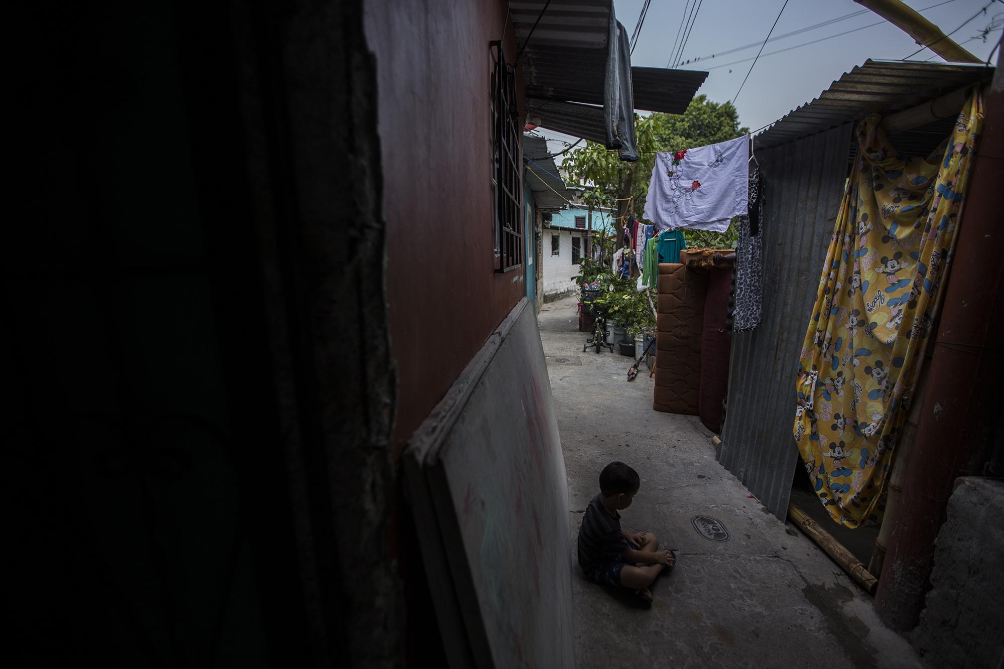 Cindy Reyes fue detenida por la Policía el 9 de abril en este pasillo, que divide su casa del baño exterior hecho de lata y bambú, en la colonia Bambular de San Salvador. Ella esperaba a que su hijo terminara de hacer sus necesidades. Lleva más de 20 días en un centro de cuarentena gubernamental. Foto de El Faro: Víctor Peña.