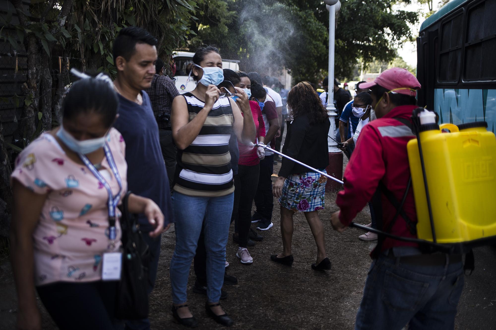 Trabajadores de la Alcaldía Municial de Panchimalco, desinfectan a los usuarios del transporte colectivo, antes de ingresar al municipio. Usan Virkon, un desinfectante mezclado con agua, y que tiene uso veterinario y para desinfectar instalaciones agroindustriales, según se lee en la etiqueta del distribuidor. Los trabajadores aseguran que es el mismo desinfectante que se utilizó para combatir el Ébola. Foto de El Faro: Víctor Peña. 