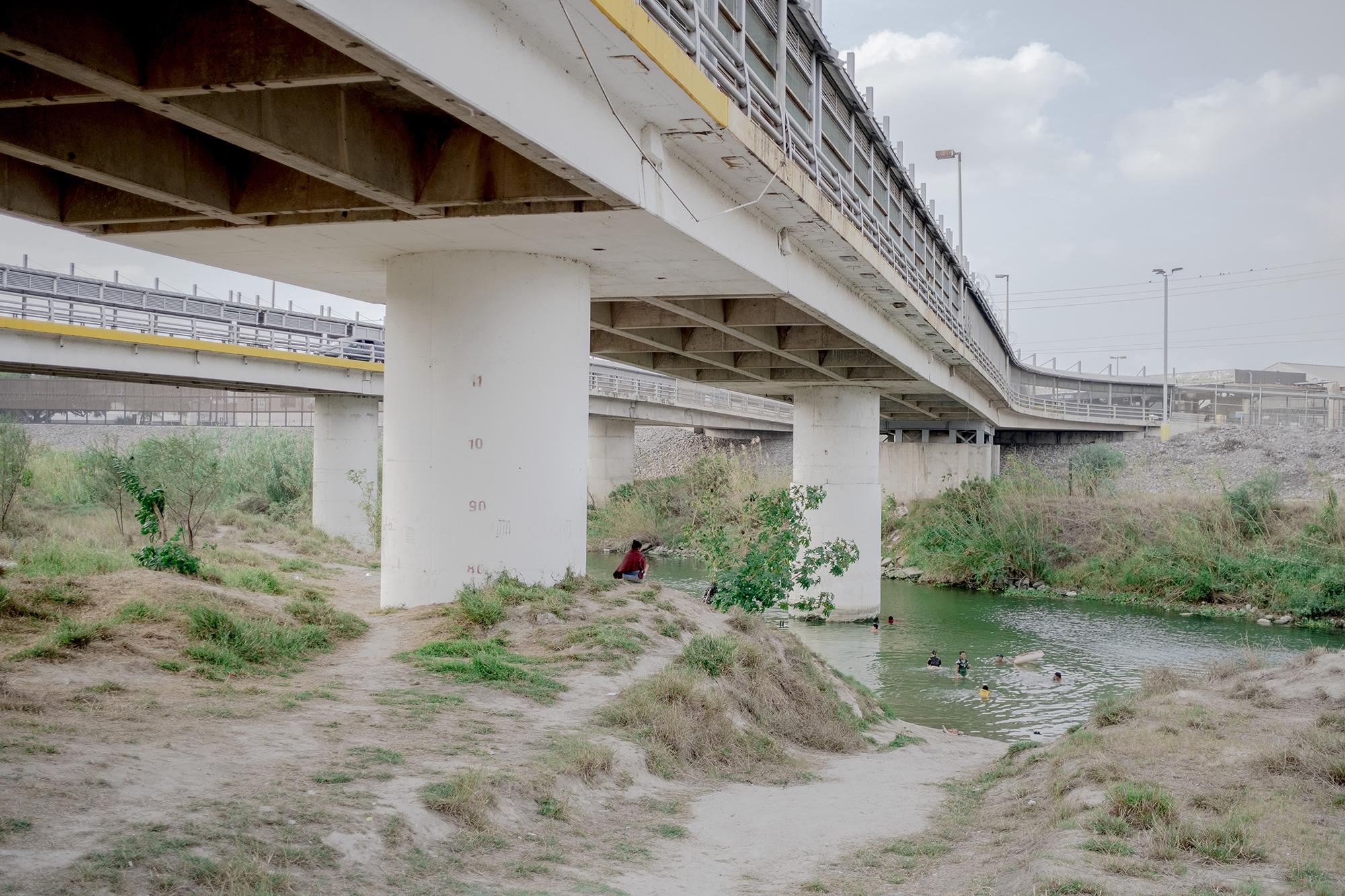 Un grupo de migrantes se baña en el río Bravo, en Matamoros, cerca del campamento. Arriba de ellos está el puente internacional que conecta con Estados Unidos, donde transitan las personas que tienen autorización legal de entrada y de salida. Mientras que por el río Bravo lo intentan los indocumentados. El coronavirus, sin embargo, no ha frenado el cruce de migrantes del todo. Foto de El Faro: Fred Ramos.