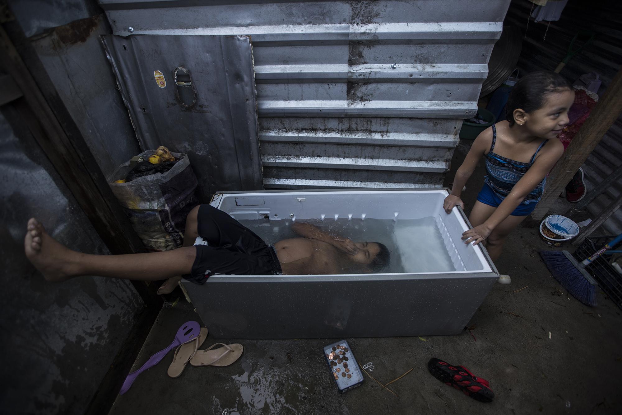 Pedro Montano, de 11 años, se sumerge en los escombros de una refrigeradora transformada en pila. Milagro, su hermana, espera su turno al interior de su vivienda en la comunidad 15 de Marzo. La casa fue construida con desechos que sus padres recogieron en la calle. Cada día, estos niños tienen derecho a una hora de recreación en su 