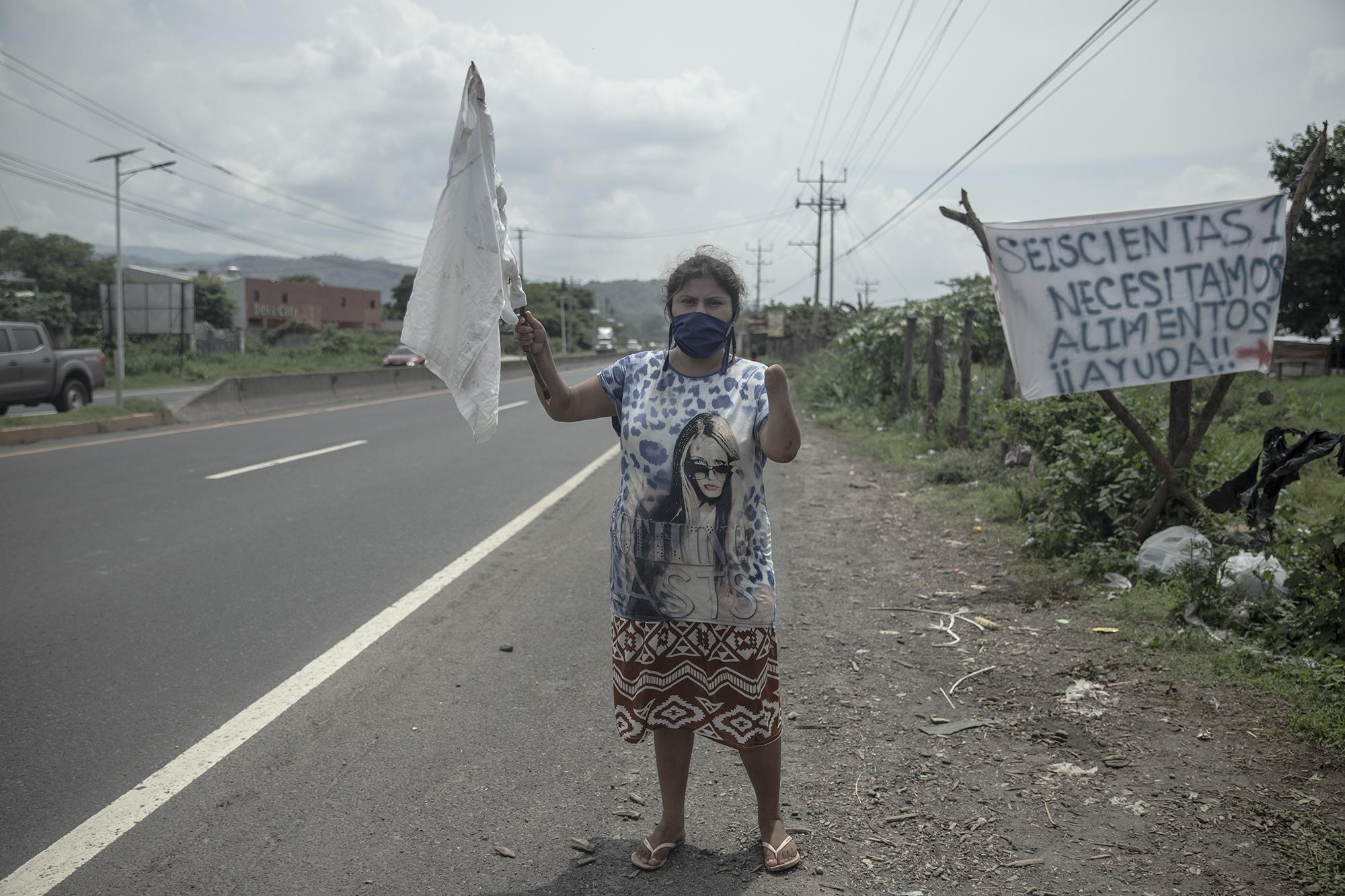 Lesly Ponce tiene 23 años de edad, todos los días sale a la carretera a Sonsonate con una bandera blanca para pedir alimentos. El lugar es conocido como Comunidad 601 y pertenece al municipio de Colón, La Libertad. Aquí, de las 30 familias, nadie recibió los $300 de ayuda del Gobierno ni la ayuda alimentaria, según asegura Lesly. Foto de El Faro: Carlos Barrera.  