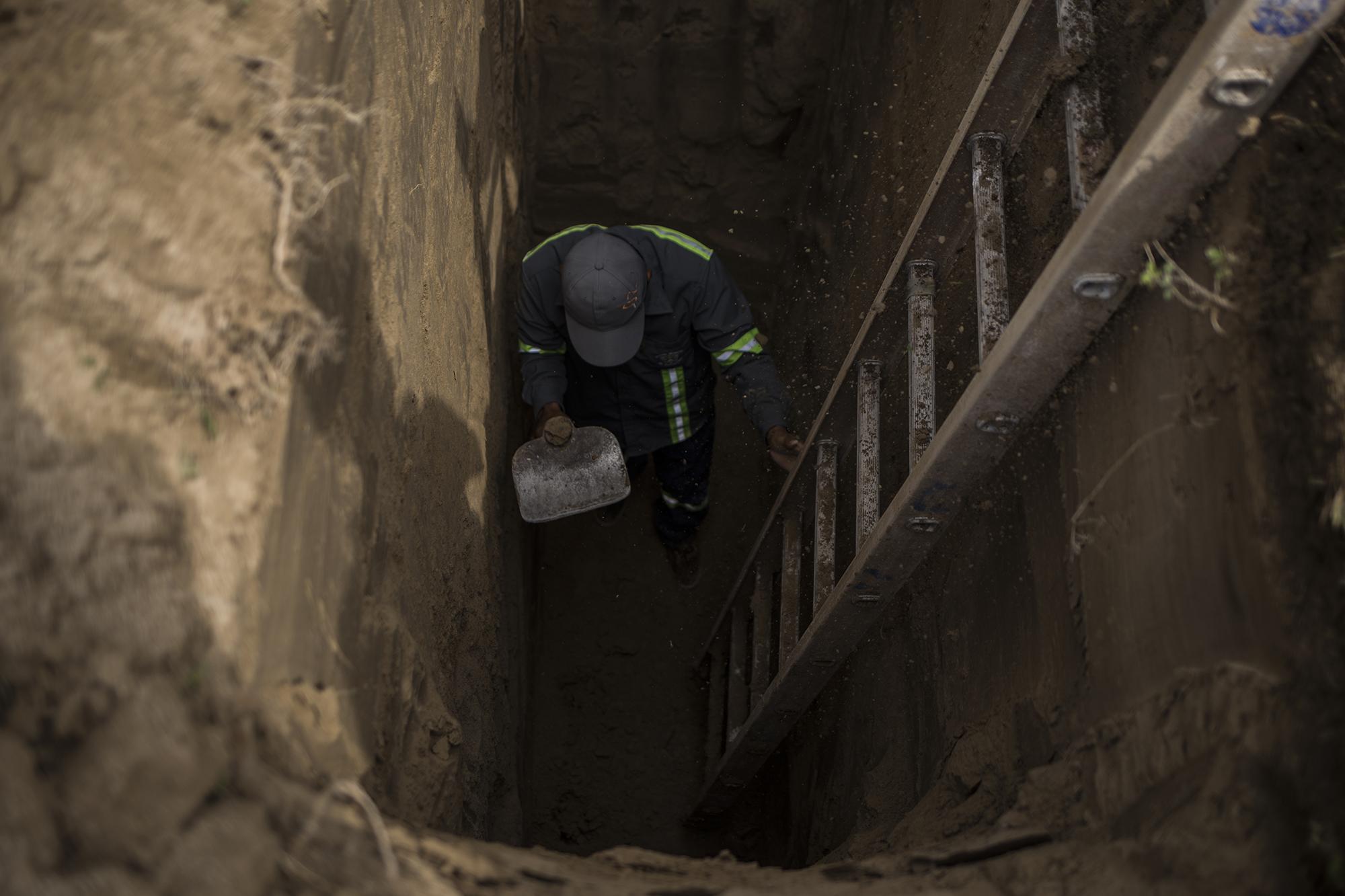 Alberto Alas, trabajador municipal del cementerio Jardín de Soyapango, retoca una de las fosas realizadas con máquina excavadora para sepultar víctimas con protocolo de covid-19. Foto de El Faro: Víctor Peña. 