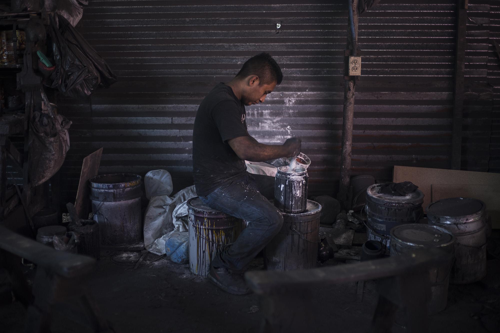 William Flores hace una mezcla de talco y thinner (solvente de pinturas). Con eso fabrica una pasta de color negro que dará firmeza a la pintura final del ataúd. William camina a diario media hora desde su casa. Recorre tres kilómetros de ida y regreso desde su casa al taller. Lo hace por veredas remotas en el cantón El Rodeo, de San Pedro Perulapán. Con la pandemia, su salario diario ha aumentado a $35. Antes ganaba entre $20 y $25 por jornada. “Muchos dicen que en esta época nos está yendo bien, pero también requiere un esfuerzo mayor”, asegura William.