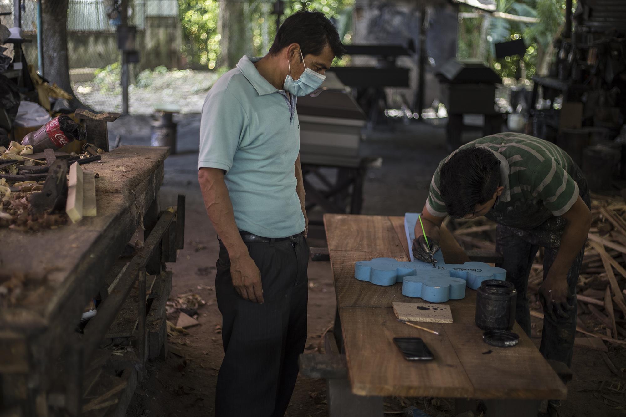 El martes 4 de agosto no había energía eléctrica. Un rayo quemó los transformadores cercanos al taller la noche anterior. La mayoría de carpinteros cortaban madera, lijaban y pintaban manualmente. Pedro (camisa celeste) estaba por comenzar un nuevo ataúd cuando llamaron al taller. Su sobrina había muerto en el hospital Médico Quirúrgico del Instituto Salvadoreño del Seguro Social. Regina Nieto murió de cáncer de colon, la enfermedad contra la que luchó los últimos dos años. El reporte médico señalaba una “sospecha de infección respiratoria aguda