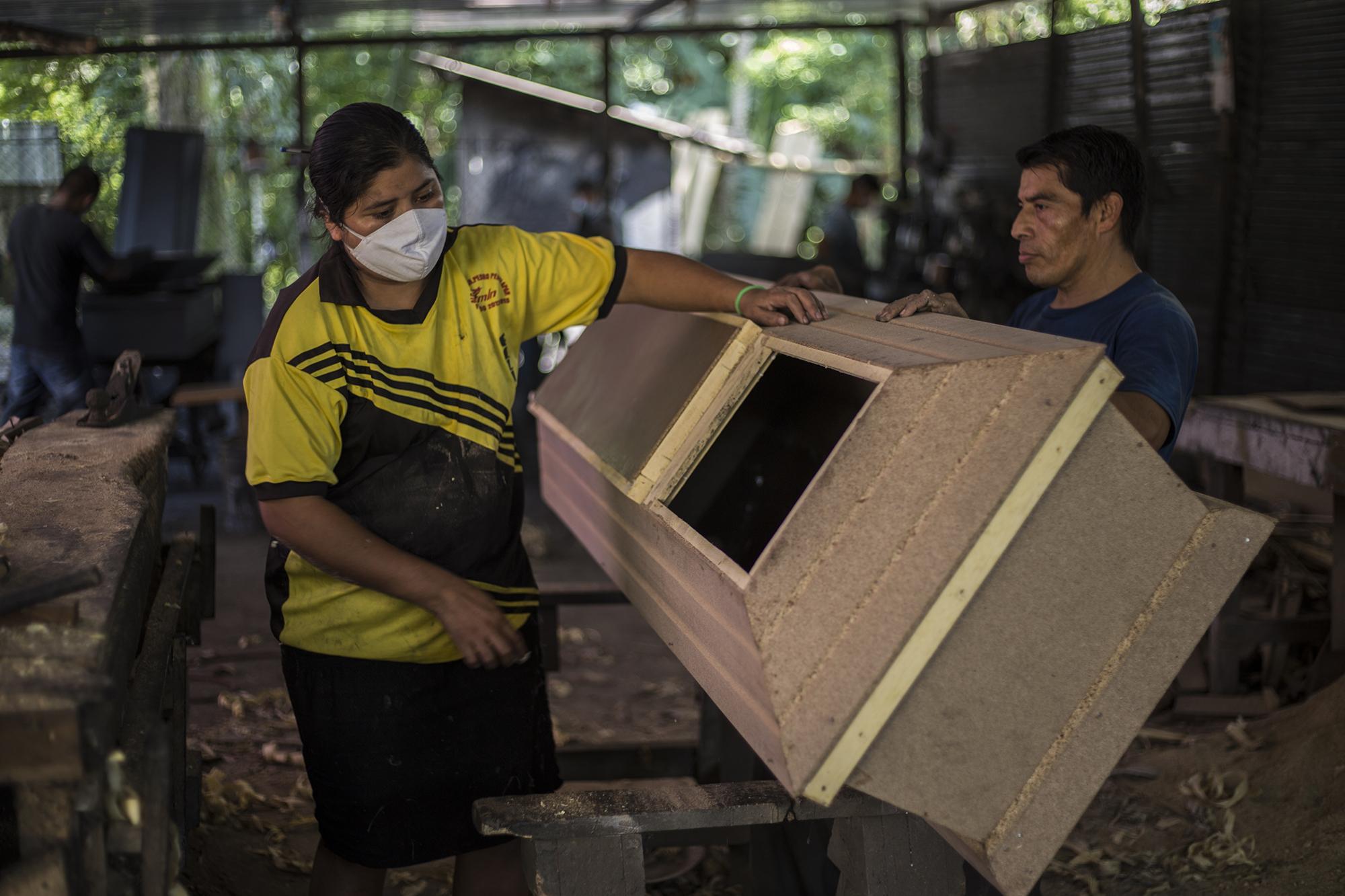 Pedro regresó al taller un día después de la muerte y el sepelio de su sobrina. Volvió a su rutina de ensamblar ataúdes y cumplir con la demanda actual.  En la imagen, Xiomara Cruz le ayuda con los últimos acabados antes de que ese féretro pase al área de pintura.