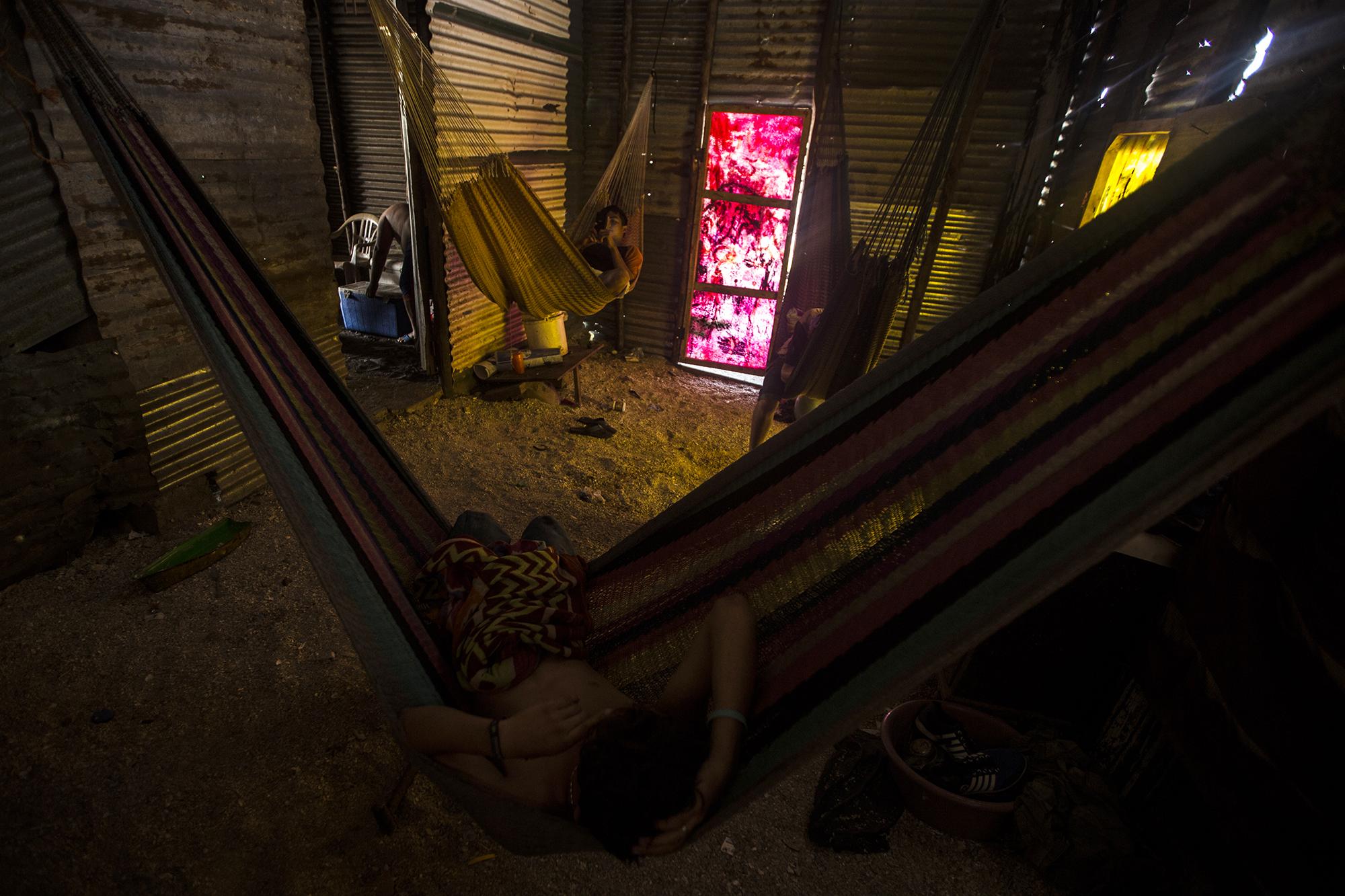 Después de su jornada de pesca, tres hermanos reposan en sus hamacas. Este es su dormitorio, sobre un piso de tierra y bajo una armazón de madera y láminas, con puertas fabricadas con fibra y resina, la misma que utilizan para elaborar sus lanchas.