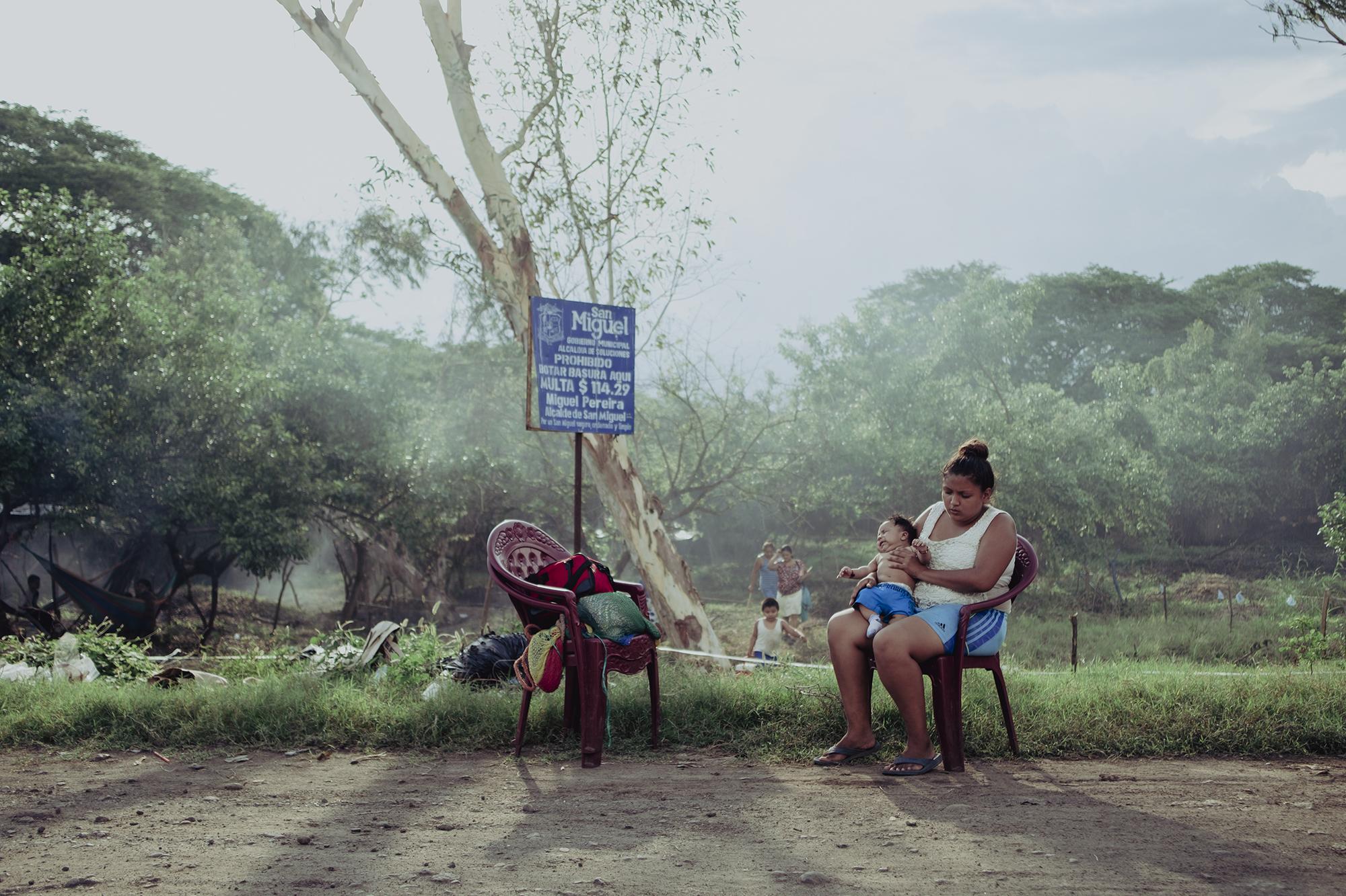 Stefany Gómez descansa junto a su hijo bajo la sombra de un árbol en el predio ubicado cerca del río Grande de San Miguel. Ella cuida del niño y su pareja lava vehículos en la ciudad. Sus ingresos son de $250 mensuales y alquilaban una pieza a $75 por mes. Durante la pandemia, ella parió a un bebé y su marido quedó desempleado. Ahora, con bebé, y el rezago económico que dejó la cuarentena, decidieron abandonar su antiguo hogar para vivir en un lugar donde puedan ahorrar el dinero y volver a empezar.