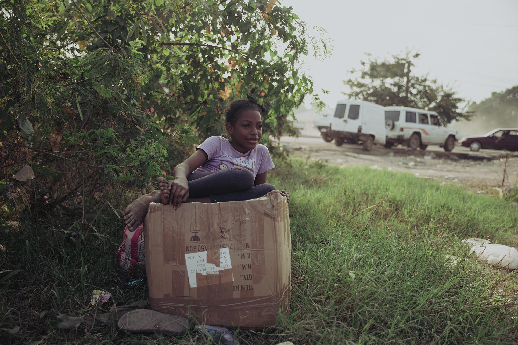 Angely Martínez espera a sus padres en la entrada de la colonia La Planeta. La Familia de Angely lo perdió todo. Ese día recibieron una caja de ropa que les regalaron particulares y sobre la que espera Angely. 