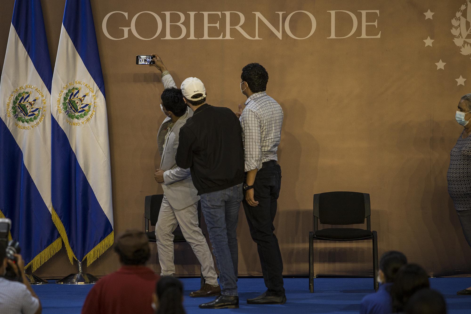 Florentín Ramos, quien compitió en las internas de Nuevas Ideas, se toma una selfie con el presidente Nayib Bukele. Sofía Romero, víctima y testigo de la masacre, observa a un costado.Foto de El Faro: Víctor Peña