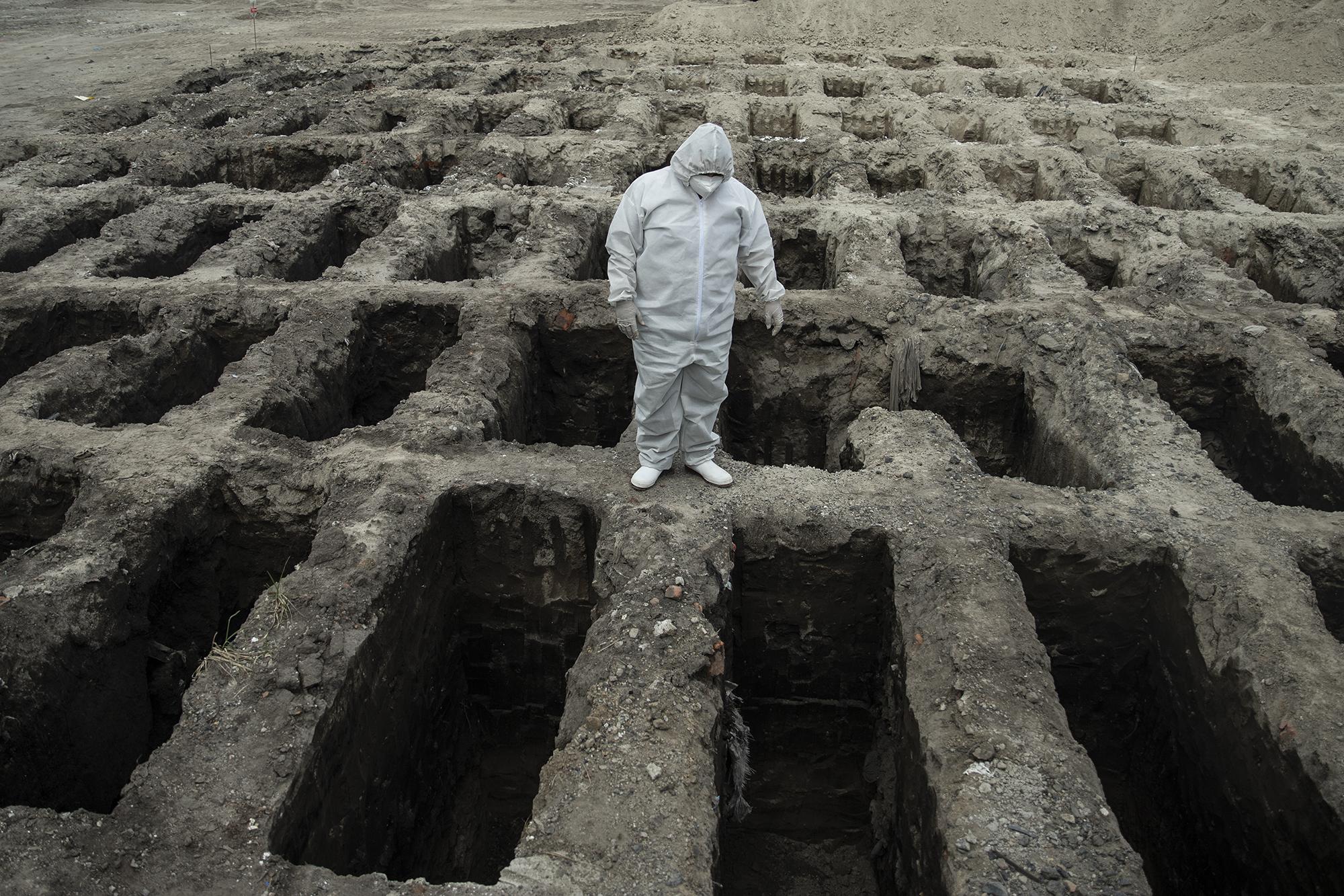 Un trabajador funerario observa el lugar donde se abrieron 84 nuevas fosas en el cementerio La Bermeja, en San Salvador, específicamente en al área dedicada a los entierros bajo protocolo covid-19. Más de 1,000 fosas fueron abiertas en ese cementerio capitalino donde se enterró a personas de diferentes municipios del área metropolitana. En los meses de junio y julio llegaron a hacerse un promedio de 20 entierros diarios en esa área del cementerio. Hasta el 20 de diciembre, la página gubernamental de divulgación sobre la pandemia reportaba a 1,250 personas fallecidas por esa causa, pero nunca ha sido un secreto que esa cifra es apenas un subregistro. Los entierros bajo las medidas de prevención del virus, que incluyen impedir que los familiares se acerquen al nicho, han sido miles en todo el país. De momento, debido a que cada municipalidad lidia con estos entierros, no hay una cifra oficial. El año cierra con un alza de casos que hace que cada día se rocen los 300 nuevos contagios registrados. La pandemia no fue cosa de 2020. Será tema principal en 2021. Foto de El Faro: Carlos Barrera. 