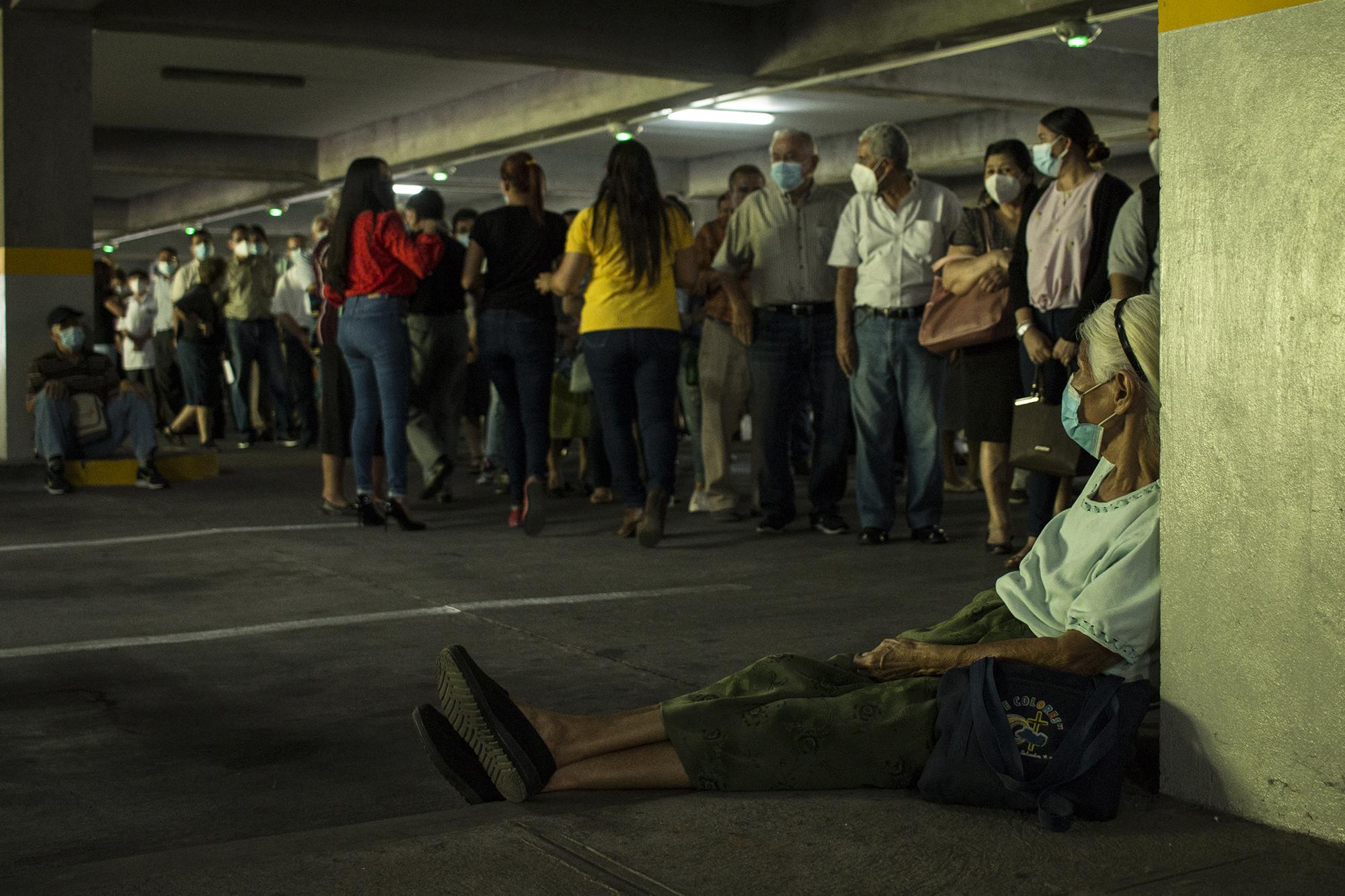 Rosario Mejía, de 80 años y habitante de San Salvador, descansa mientras llega su turno para toar un microbús hacia el Megacentro de Vacunación. Mejía esperó por dos horas en el paruqe del centro comercial. Foto de El Faro: Víctor Peña. 