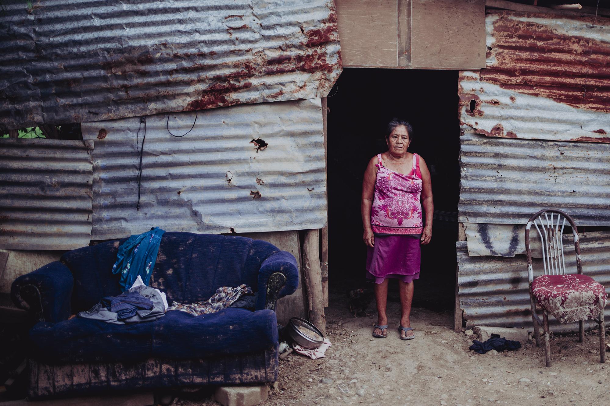 María Hernández, de 69 años de edad, frente a su champa, con las pocas cosas que el río Ulúa no se pudo llevar, un sofá y una silla. Reconstruyó su champa con láminas que el Ulúa arrastró. El día que el río se salió de su cauce, María no quería evacuar, pues no creía que el agua llegaría hasta su casa. 