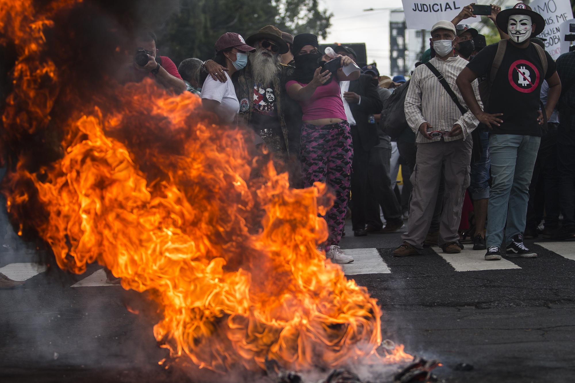 Frente al edificio de la Corte Suprema de Justicia, los protestantes incendiaron dos llantas y cajas de cartón, en rechazo a las últimas decisiones de la Sala de lo Constitucional impuesta por el Gobierno de Nayib Bukele. Detrás de una barricada, empleados del Gobierno tomaban fotografías y video a los participantes de la marcha.