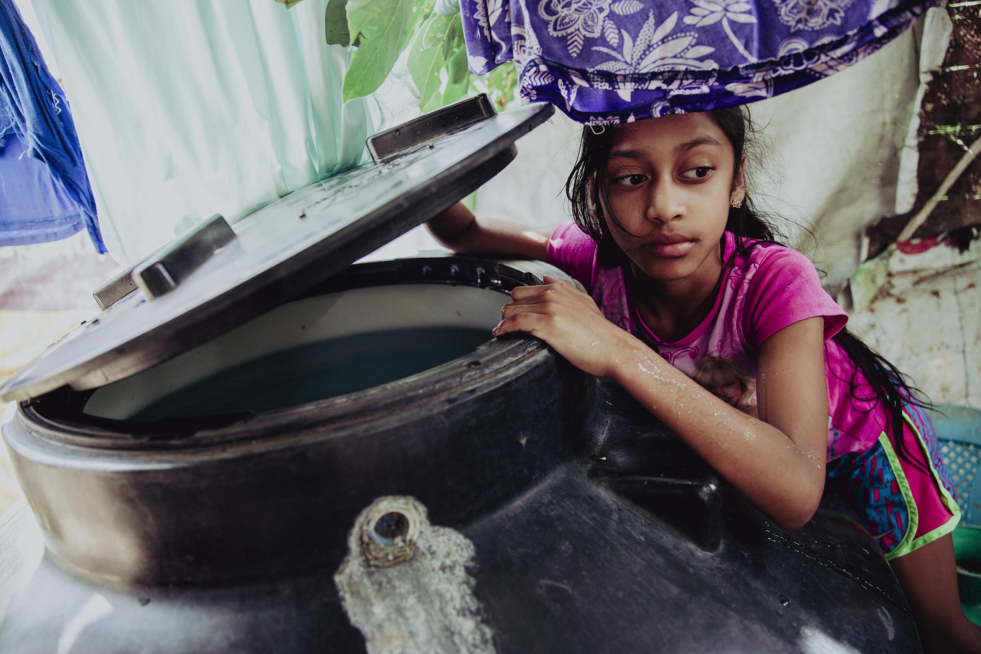 Janette Guevara, de 9 años, revisa el nivel de agua de un contenedor de su casa ubicada en el municipio de Berlín, Usulután. Los tanques y múltiples barriles son una estampa común en las casas de las comunidades del municipio y sus cantones debido a la irregularidad del servicio de agua potable. Foto de El Faro: Carlos Barrera