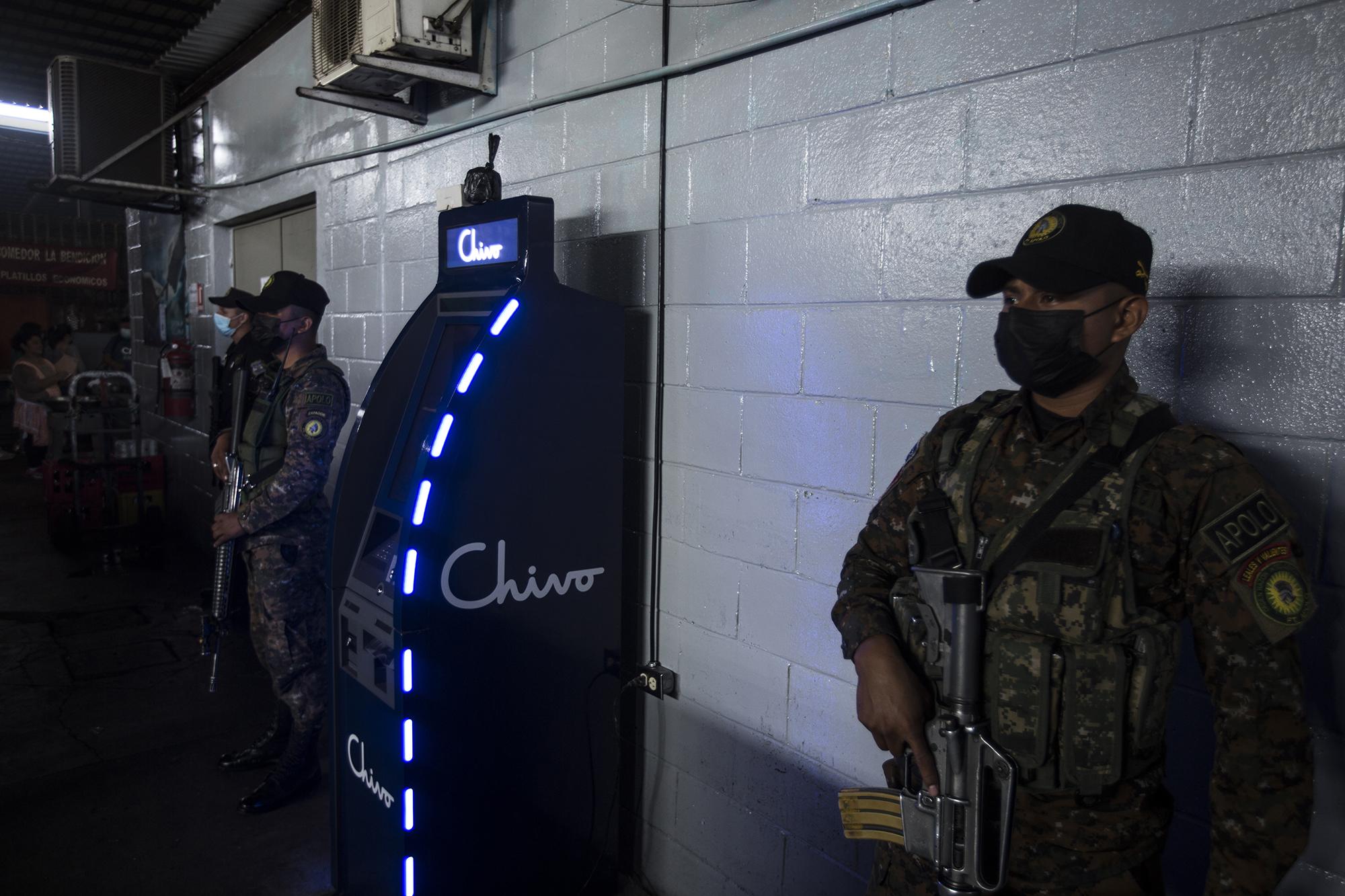 En el mes de agosto, Chivo, una empresa privada financiada con fondos del Estado, inició la instalación de los cajeros bitcoin. El Gobierno desplegó un amplio operativo militar y policial por todo el país para cuidar las casetas y cajeros. En la imagen, militares custodian uno de esos cajeros instalados en el mercado municipal de Santa Tecla, en el departamento de La Libertad. Foto de El Faro: Víctor Peña.