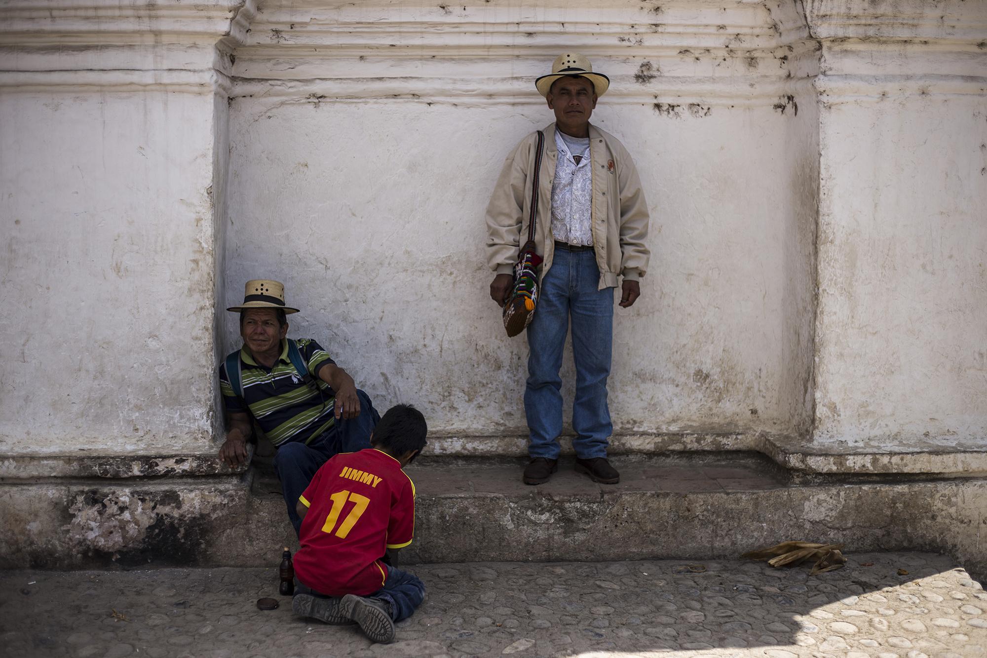 Gaspar Caba (left), 50, and Miguel Brito, 42, rest at the entrance to the church in the municipality of Chajul, while a young boy shines their shoes. Communities in the area live in conditions of extreme poverty.