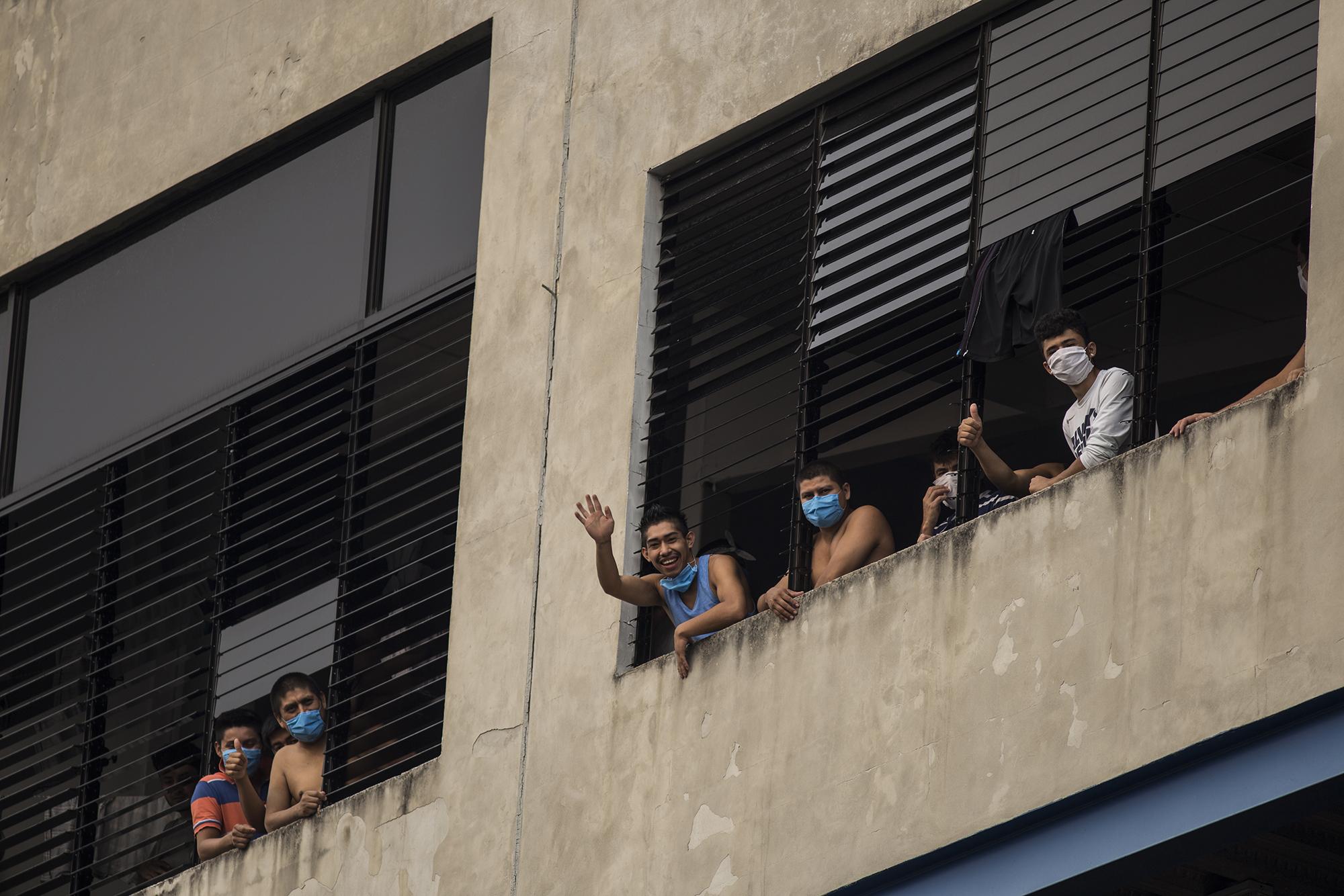 Algunas personas retenidas por supuestamente incumplir la cuarentena saludan la tarde del 27 de abril desde las ventanas del edificio Gamaliel, del Tabernáculo Bíblico Bautista Amigos de Israel, sobre la 75 Avenida Sur y Avenida Olímpica, en San Salvador. Algunos de los retenidos ahí se han quejado de que un grupo de personas golpea a otros detenidos mientras se emborrachan. Foto de El Faro: Víctor Peña. 