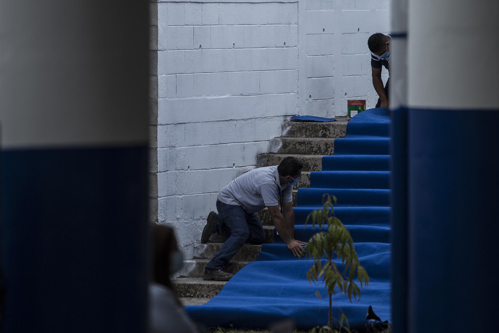 Empleados de Casa Presidencial colocan la alfombra para el recorrido, previo a la llegada del presidente Bukele al Complejo Educativo del caserío El Mozote, en Morazán. Foto de El Faro: Víctor Peña. 