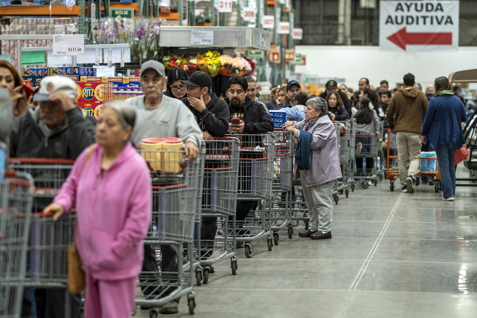 Los clientes que compran principalmente papel higiénico, toallitas de limpieza y agua embotellada, hacen cola para pagar en una tienda mayorista ante la pandemia mundial de coronavirus COVID-19 en Tijuana, estado de Baja California, México, el 13 de marzo de 2020. (Foto de Guillermo Arias / AFP)